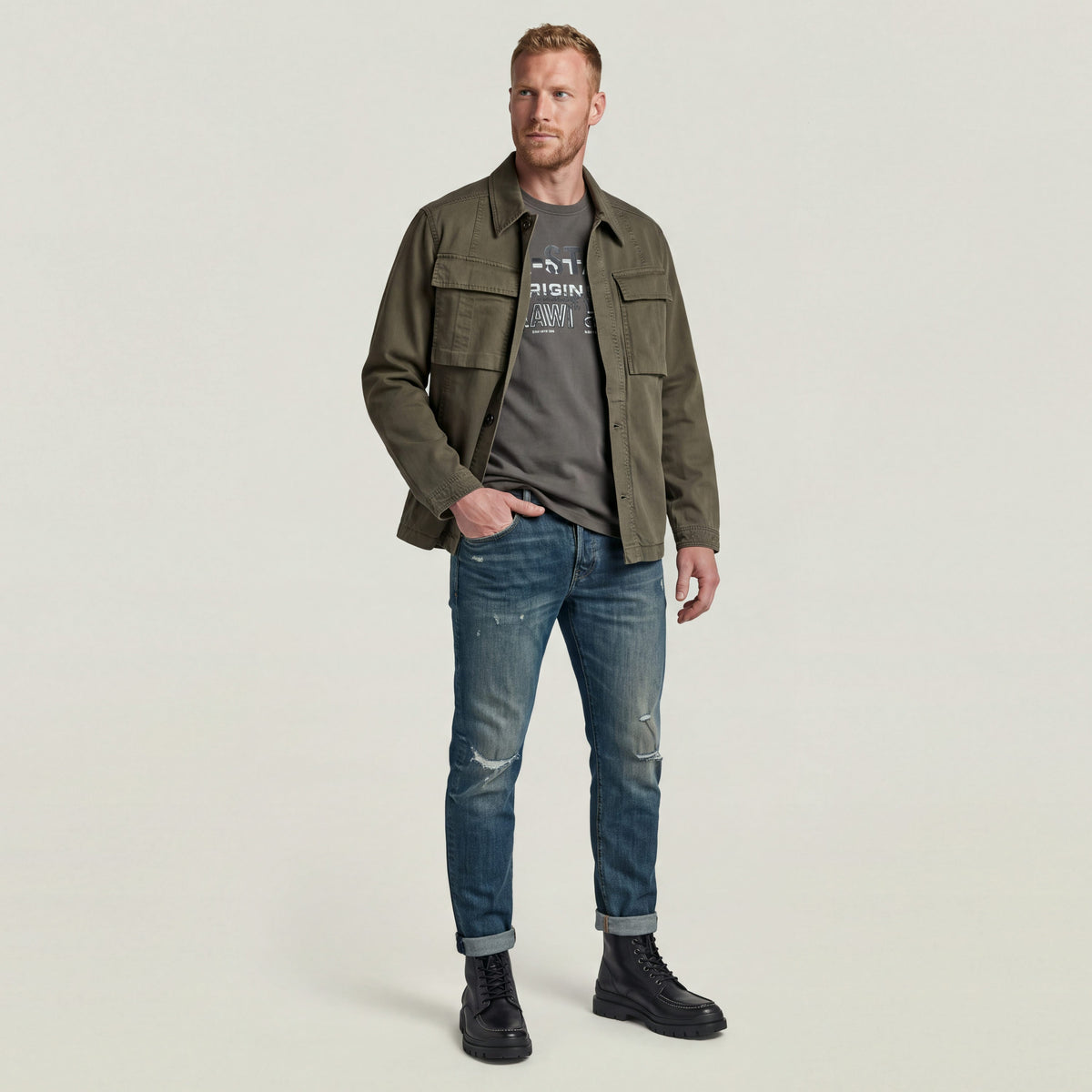 Hombre vistiendo 3301 slim fit jeans con camiseta gris y chaqueta verde, estilo casual moderno.