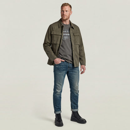 Hombre vistiendo 3301 slim fit jeans con camiseta gris y chaqueta verde, estilo casual moderno.