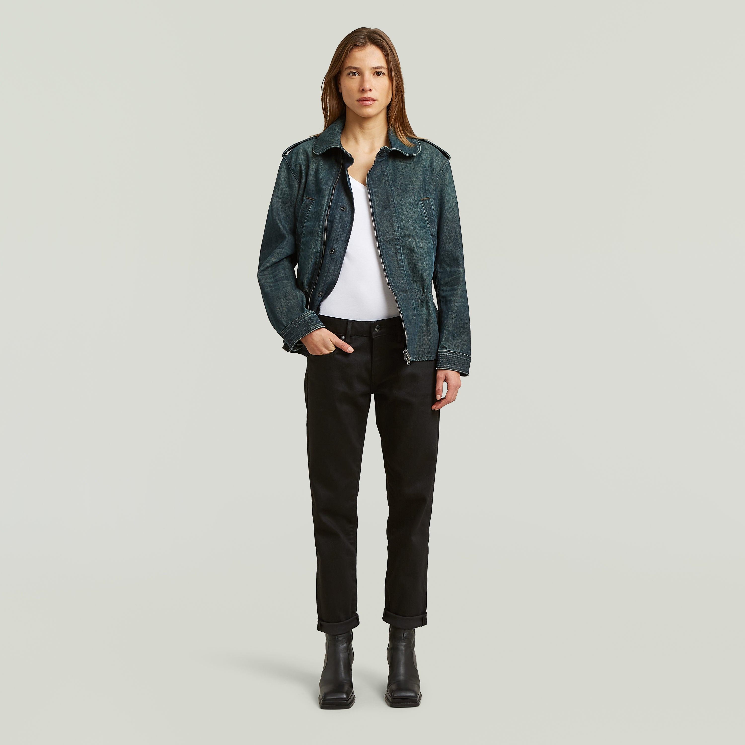 Mujer modelando jeans boyfriend style raw denim jeans con chaqueta de mezclilla y botas negras.