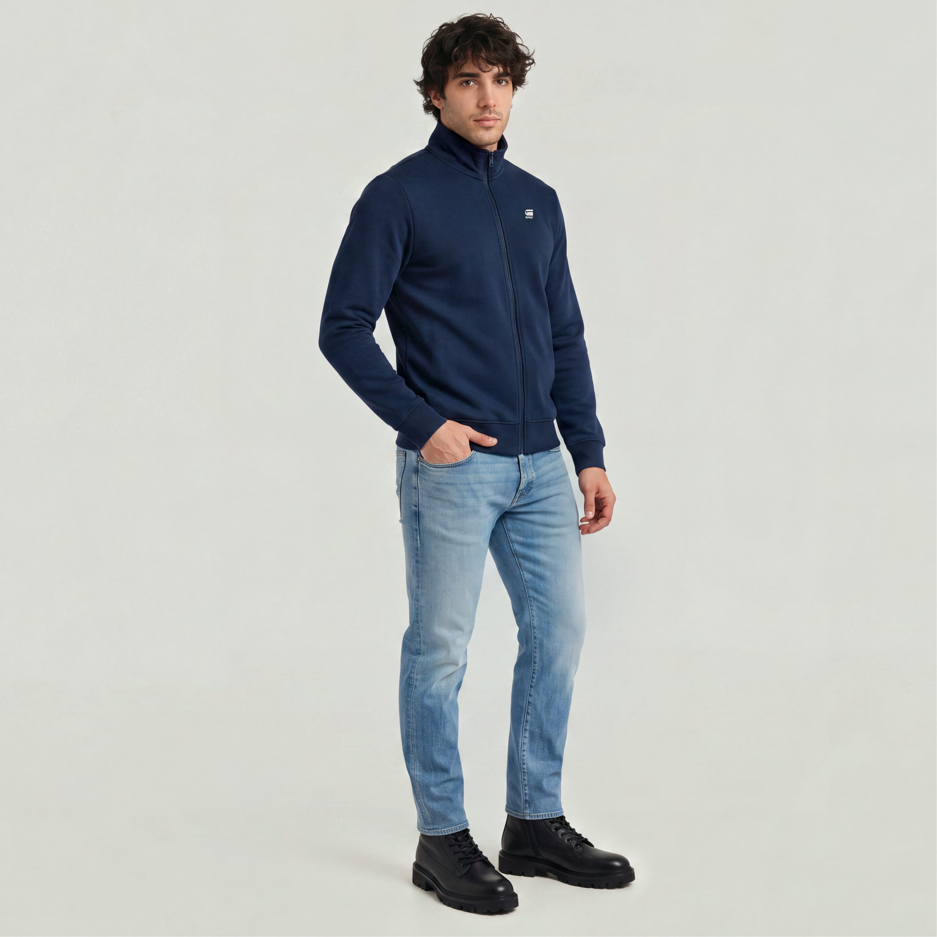 Slim tapered jeans for men paired with a navy zip jacket and black boots, showcasing a modern casual style.