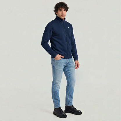 Slim tapered jeans for men paired with a navy zip jacket and black boots, showcasing a modern casual style.