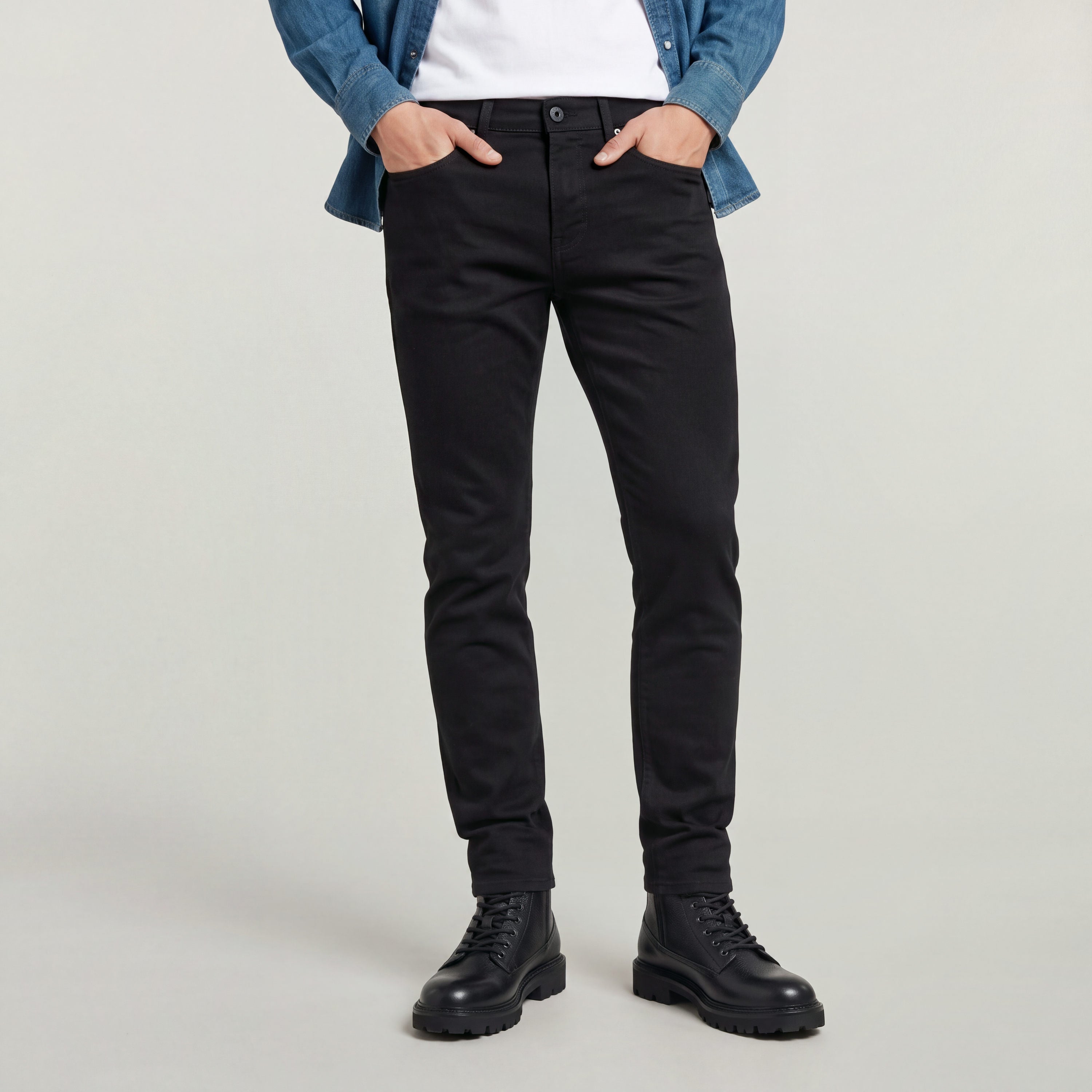 Hombre usando los jeans Streem Slim Tapered raw jeans, corte ajustado en color negro con camiseta blanca y camisa de mezclilla.