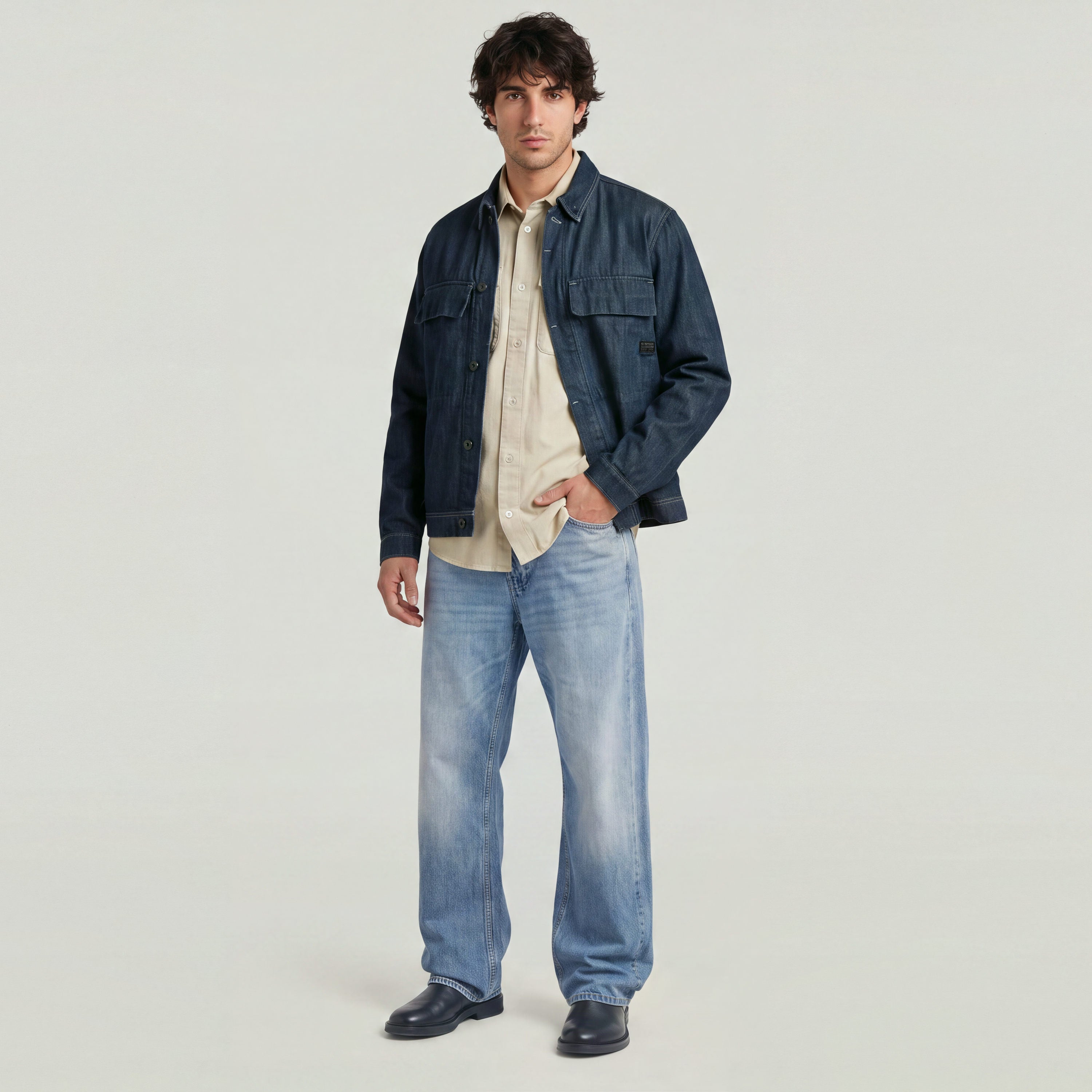 Model wearing boxy clean denim overshirt with blue jeans in a minimalist setting.