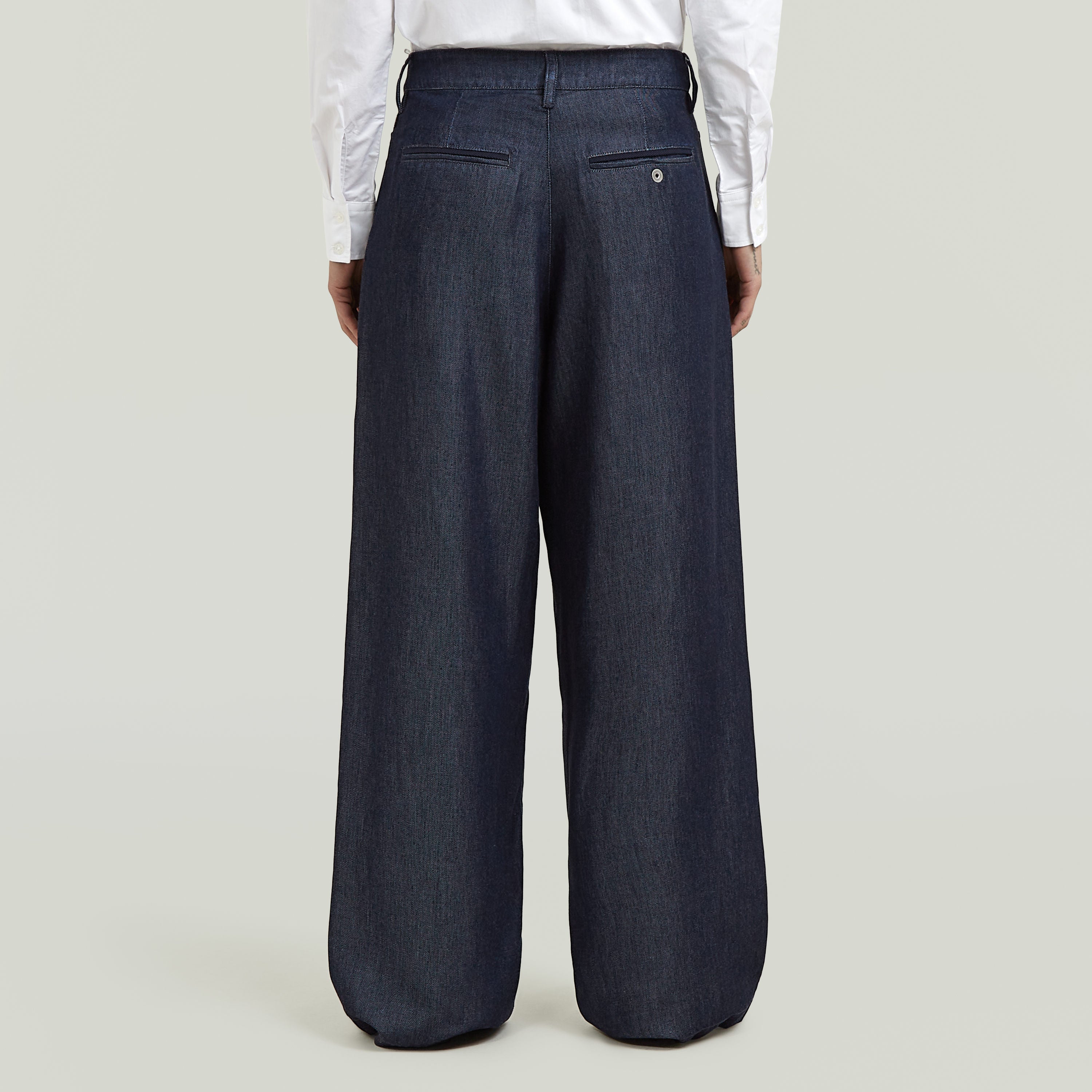 Vista trasera de pantalones pleated chino pants en color oscuro, con detalles de bolsillo y ajuste amplio.