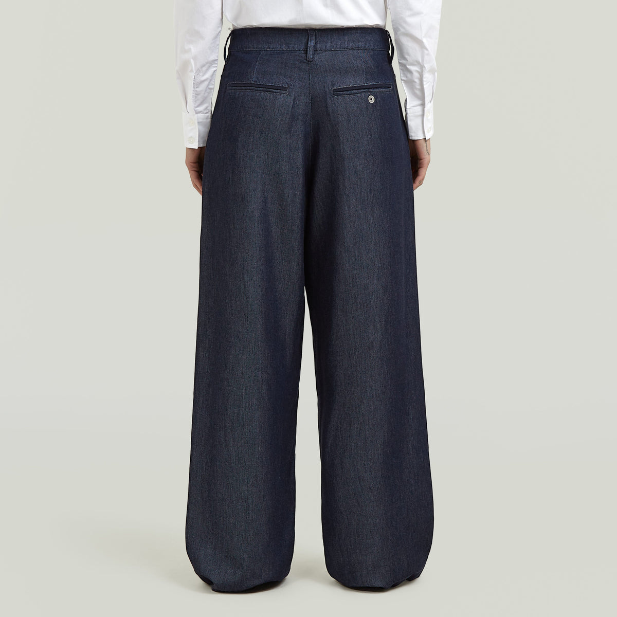 Vista trasera de pantalones pleated chino pants en color oscuro, con detalles de bolsillo y ajuste amplio.