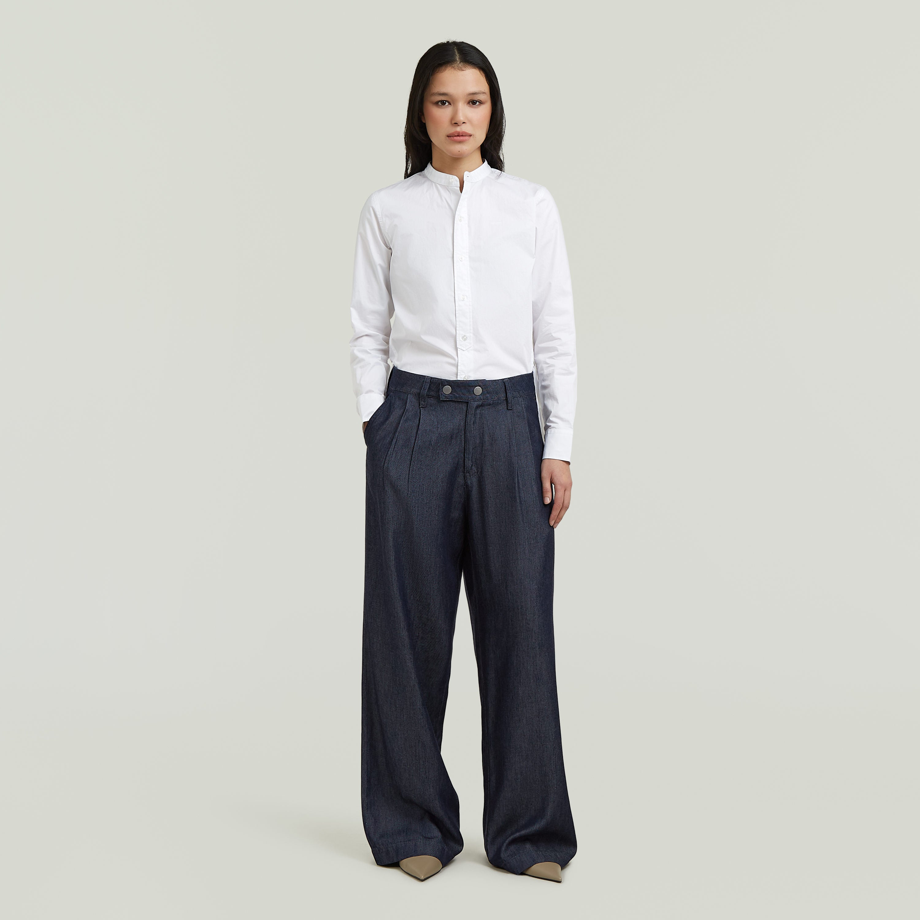 Mujer vistiendo pleated chino pants de corte recto con camisa blanca en fondo claro.