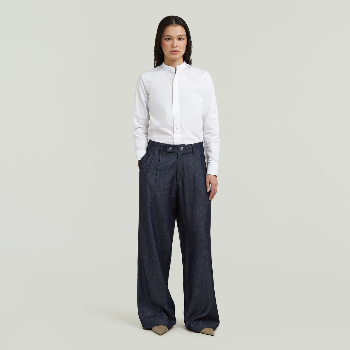 Mujer vistiendo pleated chino pants de corte recto con camisa blanca en fondo claro.