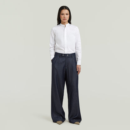 Mujer vistiendo pleated chino pants de corte recto con camisa blanca en fondo claro.