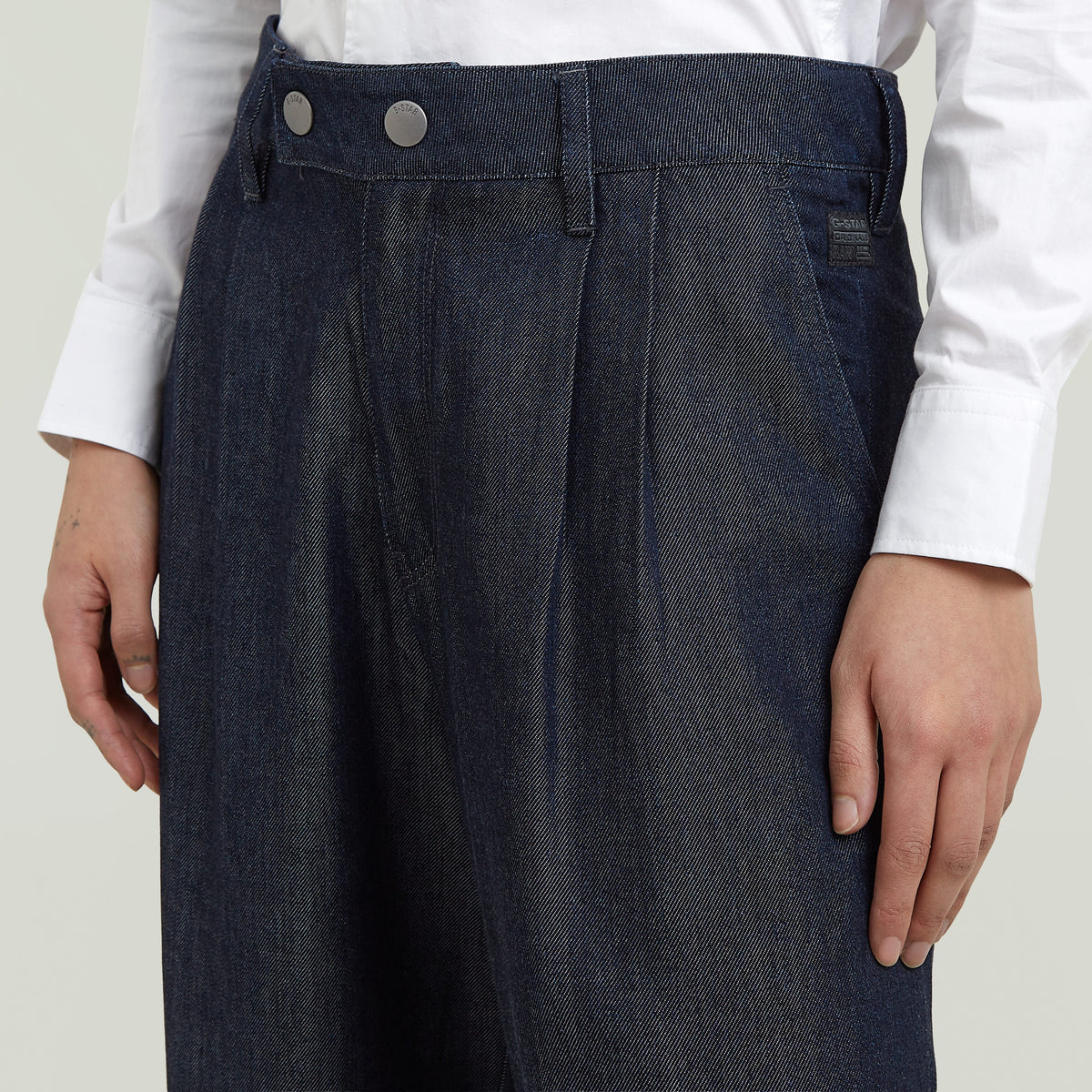 Close-up of pleated chino pants featuring a medium rise, front pockets, and modern stitching detail.