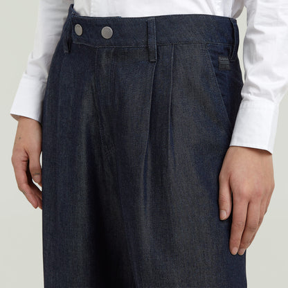 Close-up of pleated chino pants featuring a medium rise, front pockets, and modern stitching detail.
