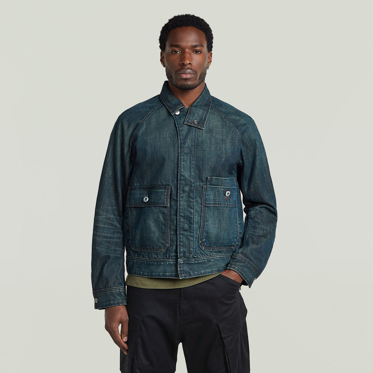 Man wearing a classic battle denim jacket with a straight cut and chest flap pocket, showcasing unique greenish indigo denim.