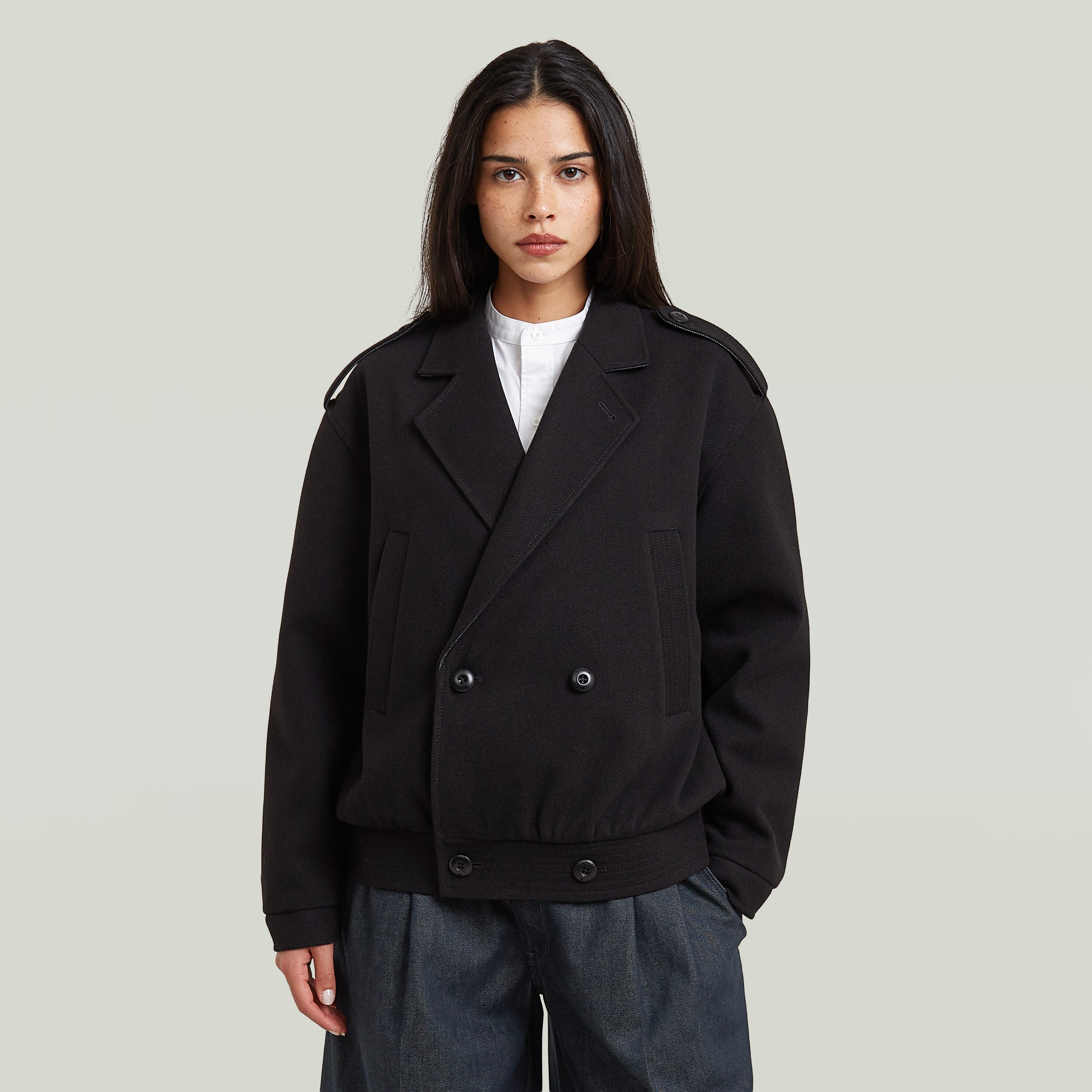 Gabardina bomber corta de mujer en color negro con cierre de botones y cuello con solapa, estilo moderno.