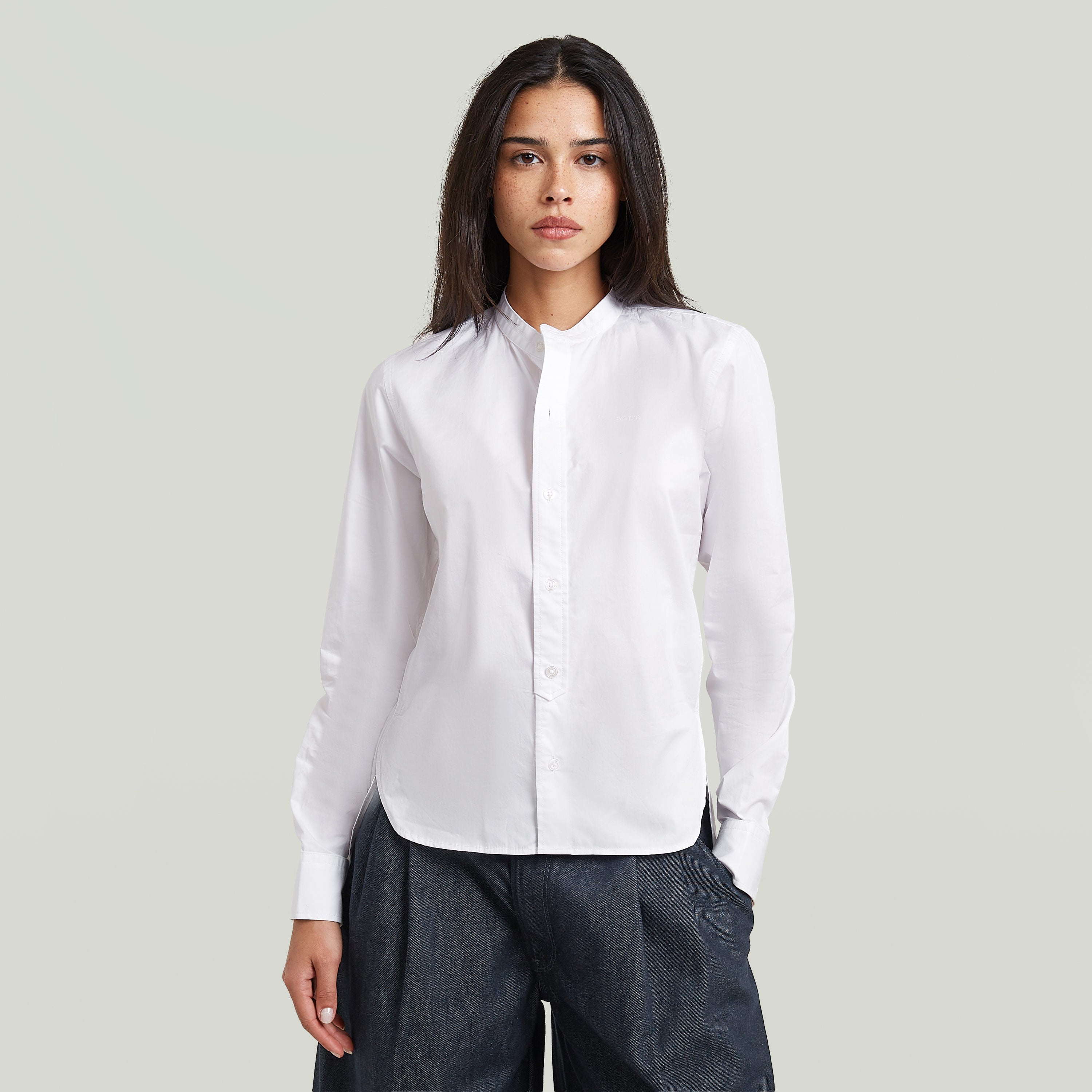 Woman wearing a classic button-up long sleeve shirt in white with a high collar.