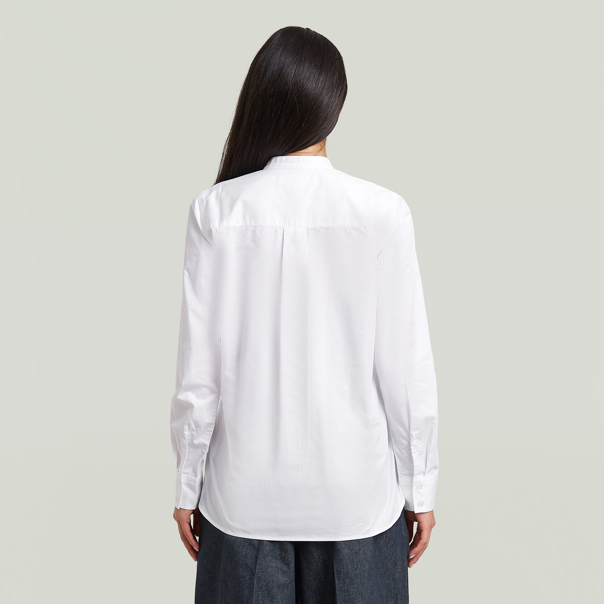 Back view of a woman wearing a classic button-up long sleeve shirt, showcasing its elegant design and button closure.