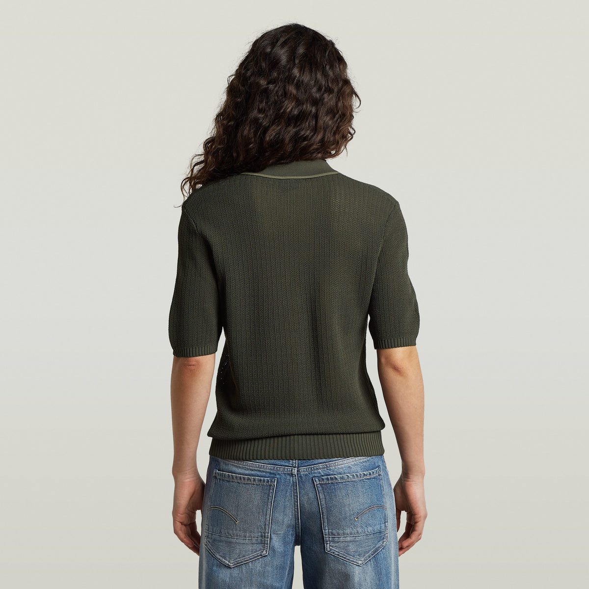 Back view of a woman wearing a classic knit polo shirt in olive green with short sleeves.