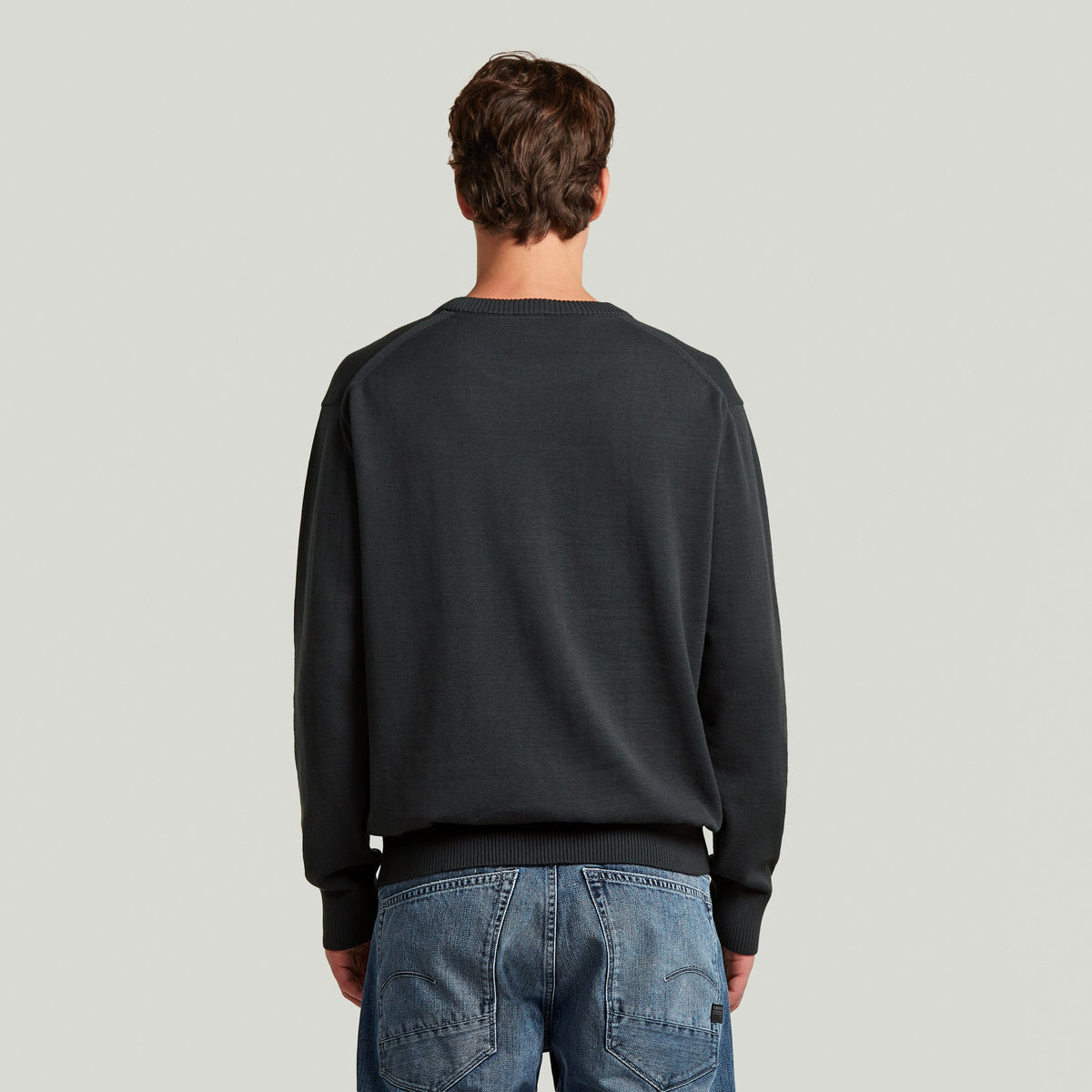 Hombre de espaldas vistiendo un classic knit pullover de color oscuro con detalles clásicos y mangas largas.