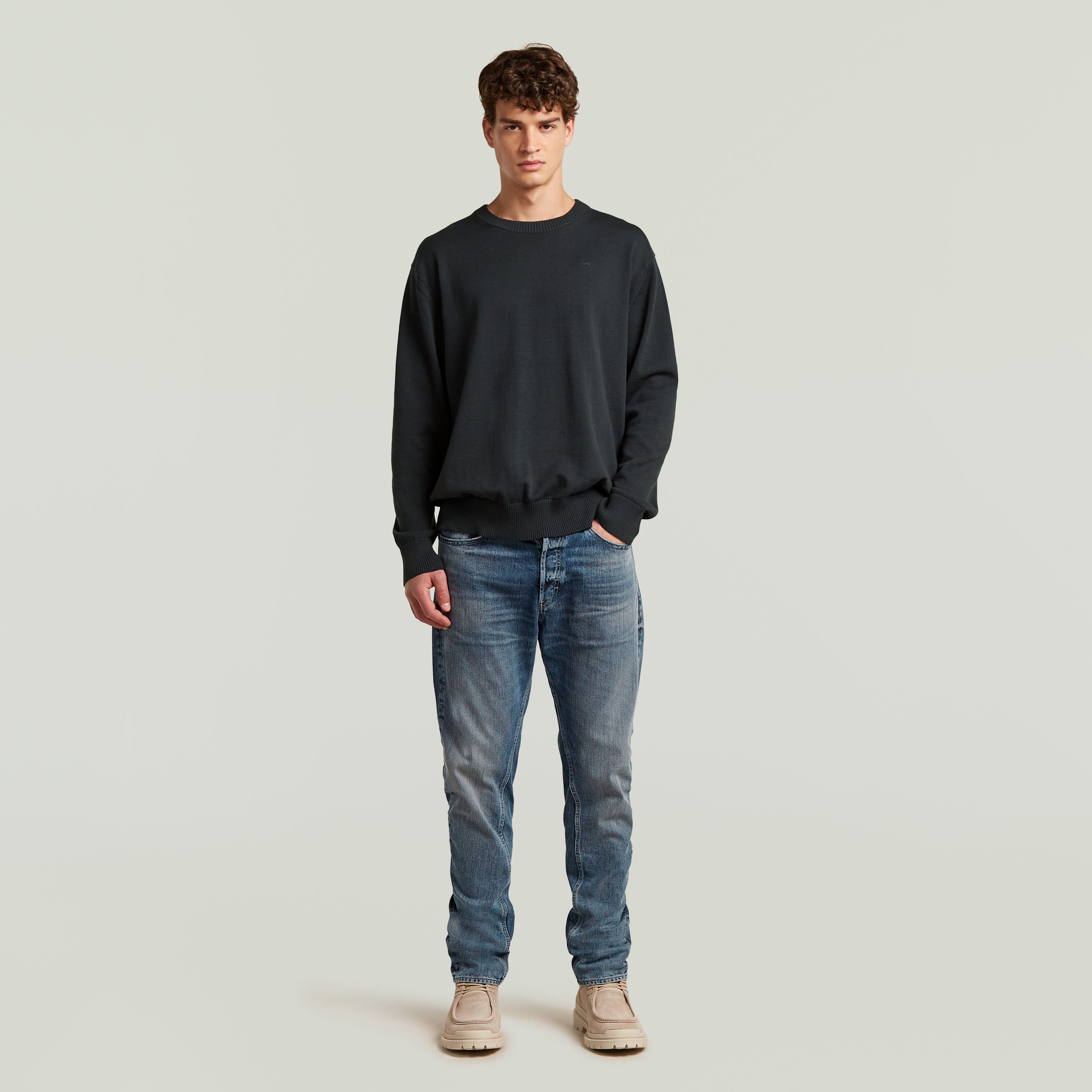 Man wearing a classic knit pullover with jeans, showcasing a timeless wardrobe essential.