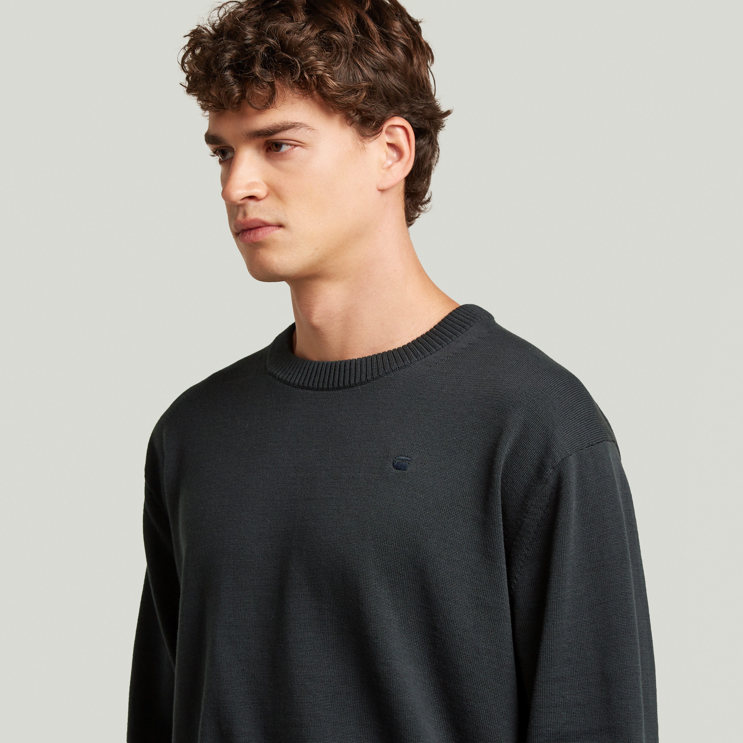 Modelo vistiendo un classic knit pullover de color oscuro, con cuello redondo y manga larga.