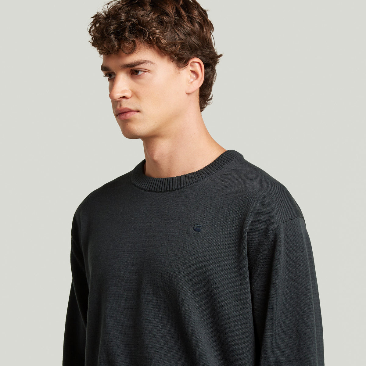 Modelo vistiendo un classic knit pullover de color oscuro, con cuello redondo y manga larga.
