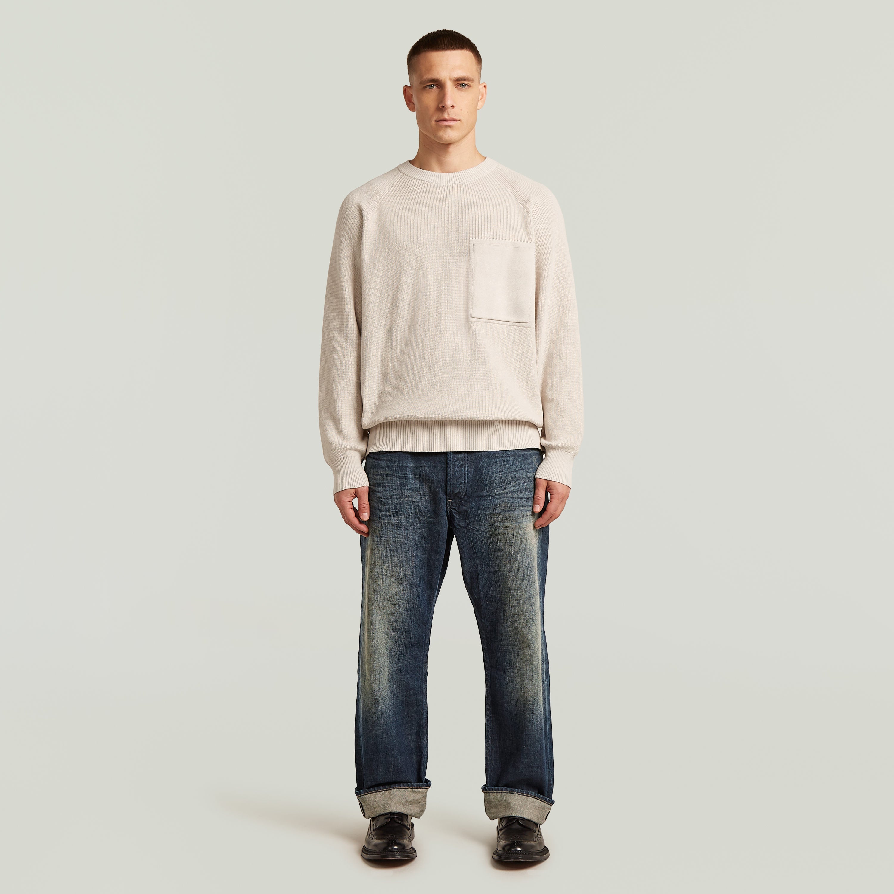 Hombre usando un jersey de punto Raglan Rib Pocket Knit de color crema con bolsillo acanalado.