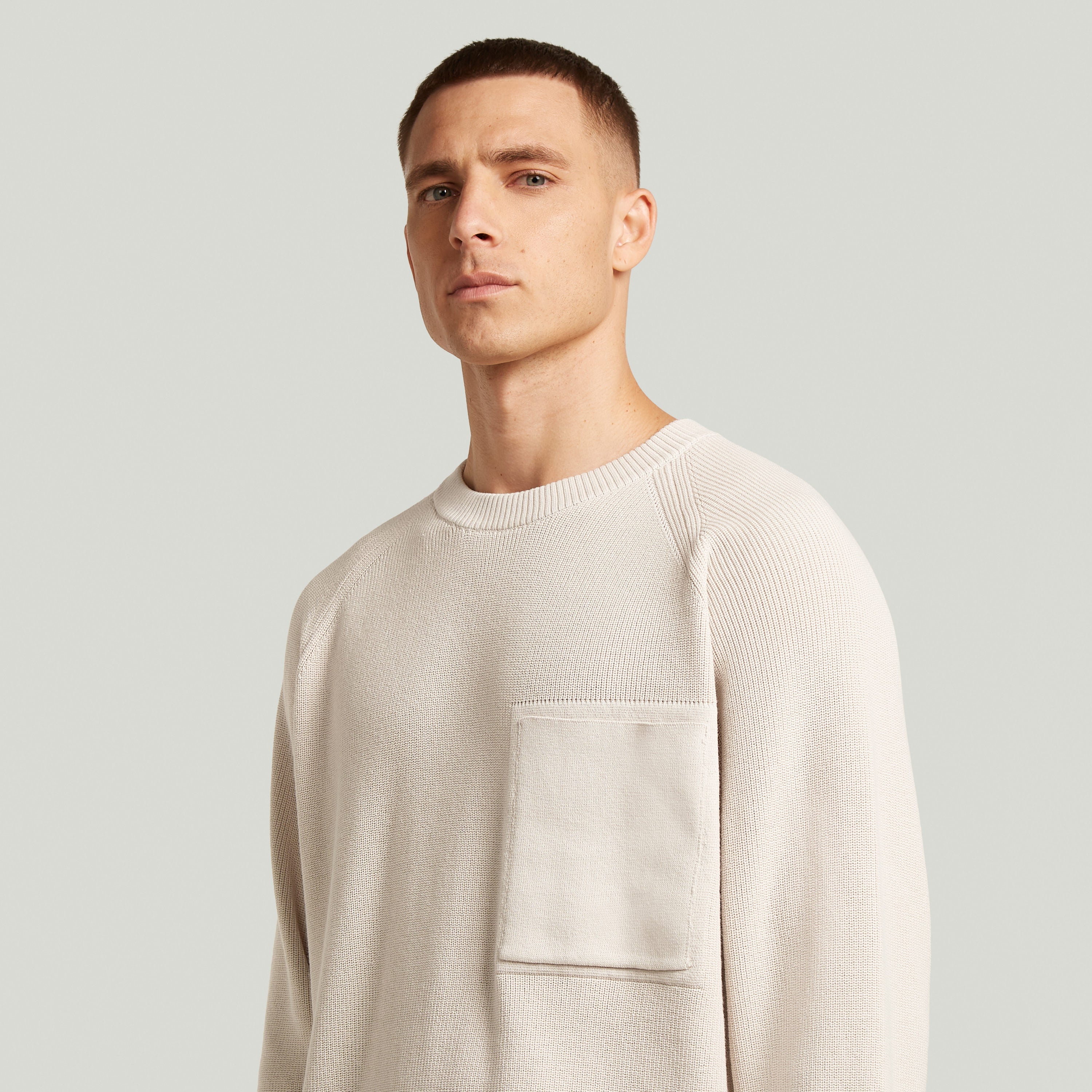 Hombre luciendo un jersey de punto con bolsillo acanalado, estilo raglan rib pocket knit, corte regular y mangas largas.