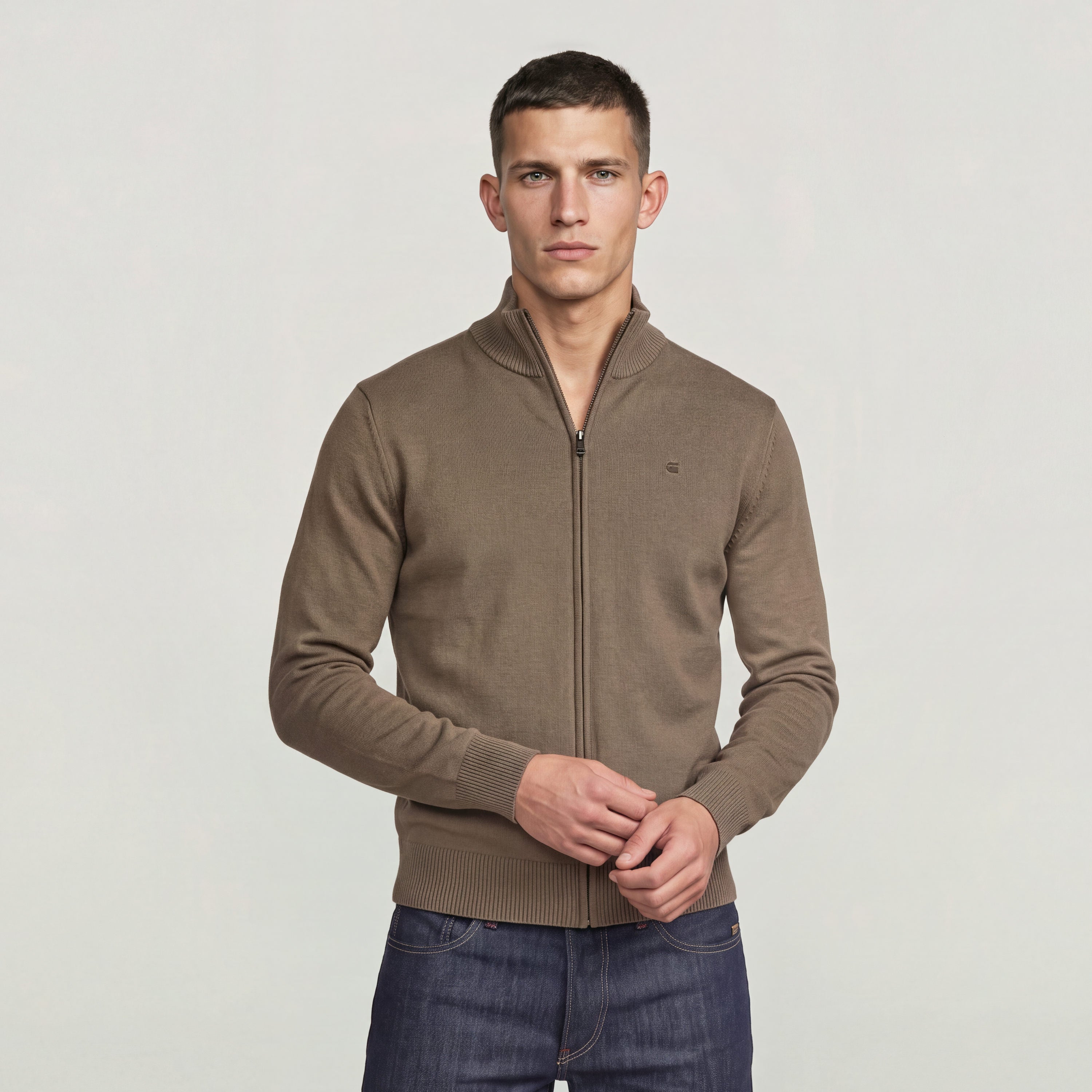 Hombre usando el Core Refined Full Zip Knit en color marrón, con cierre de cremallera y cuello alzado.