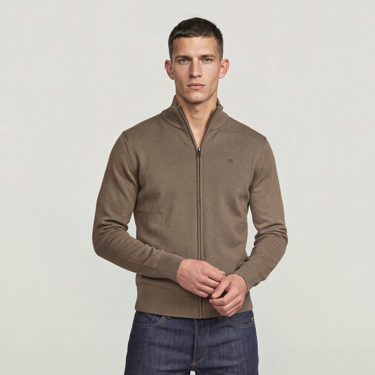 Hombre usando el Core Refined Full Zip Knit en color marrón, con cierre de cremallera y cuello alzado.