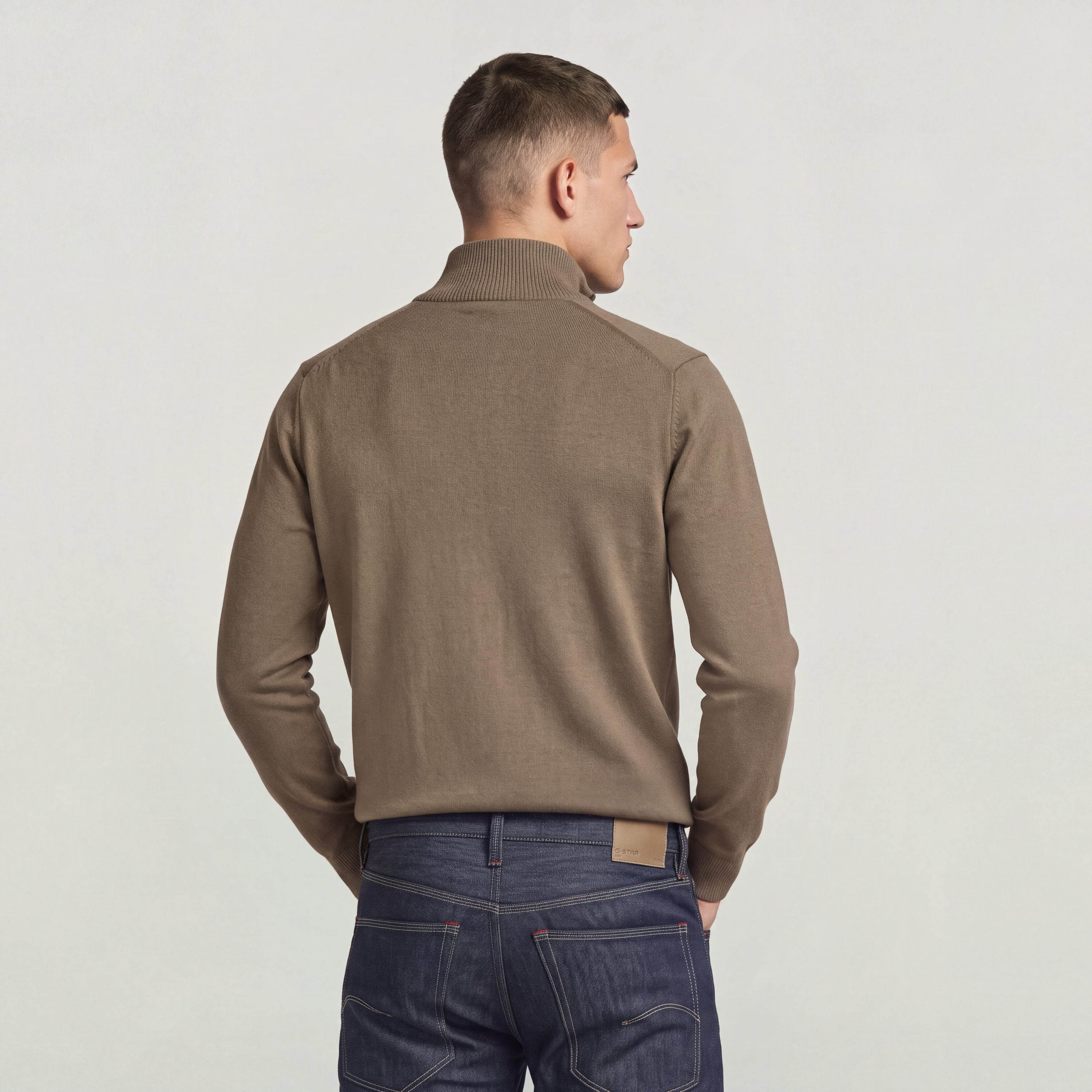 Back view of a model wearing the core refined full zip knit in a stylish brown color.