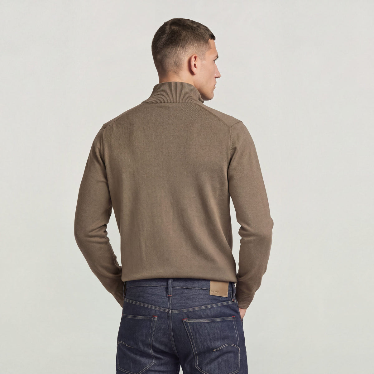 Back view of a model wearing the core refined full zip knit in a stylish brown color.