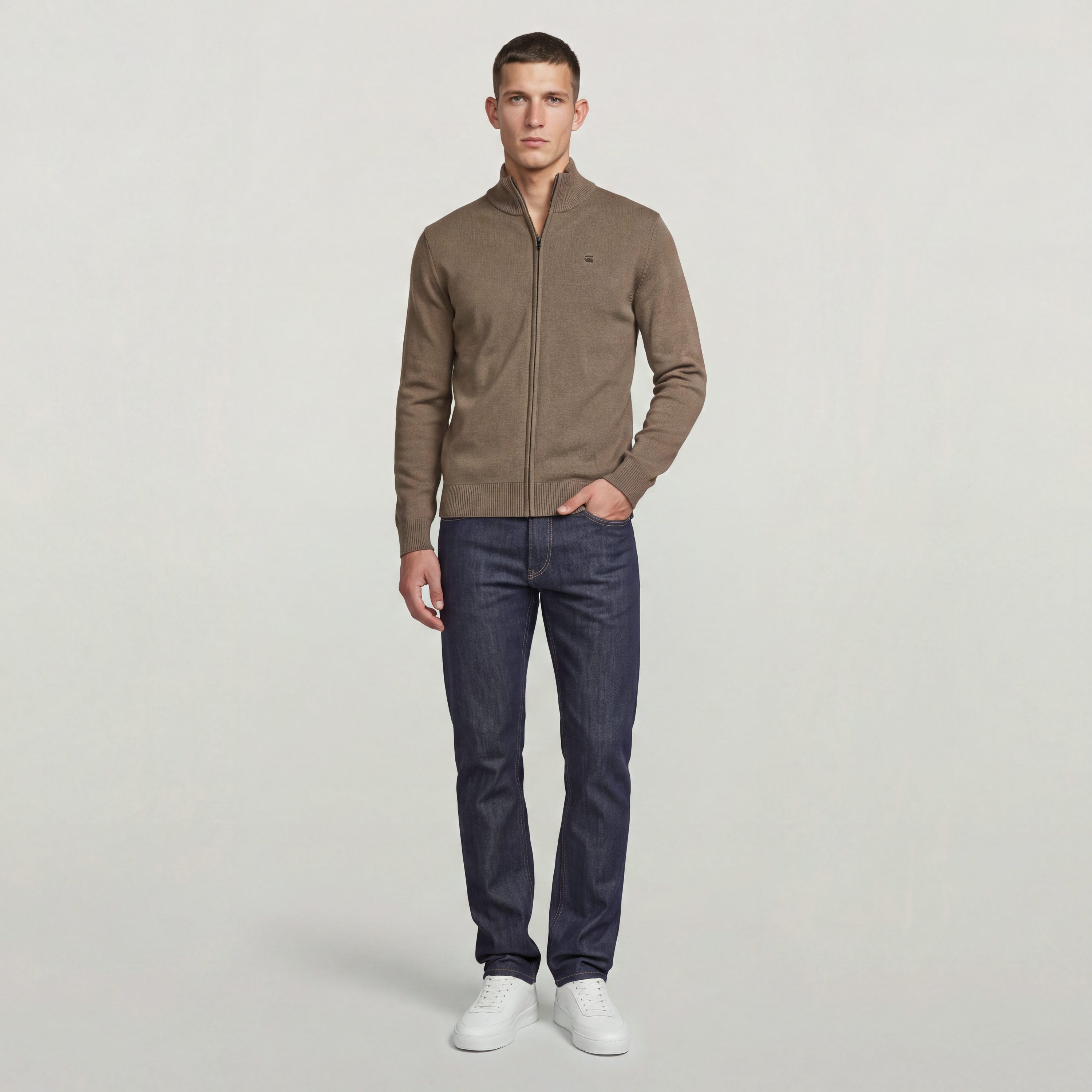 Hombre usando el Core Refined Full Zip Knit en color marrón con jeans oscuros y zapatillas blancas.
