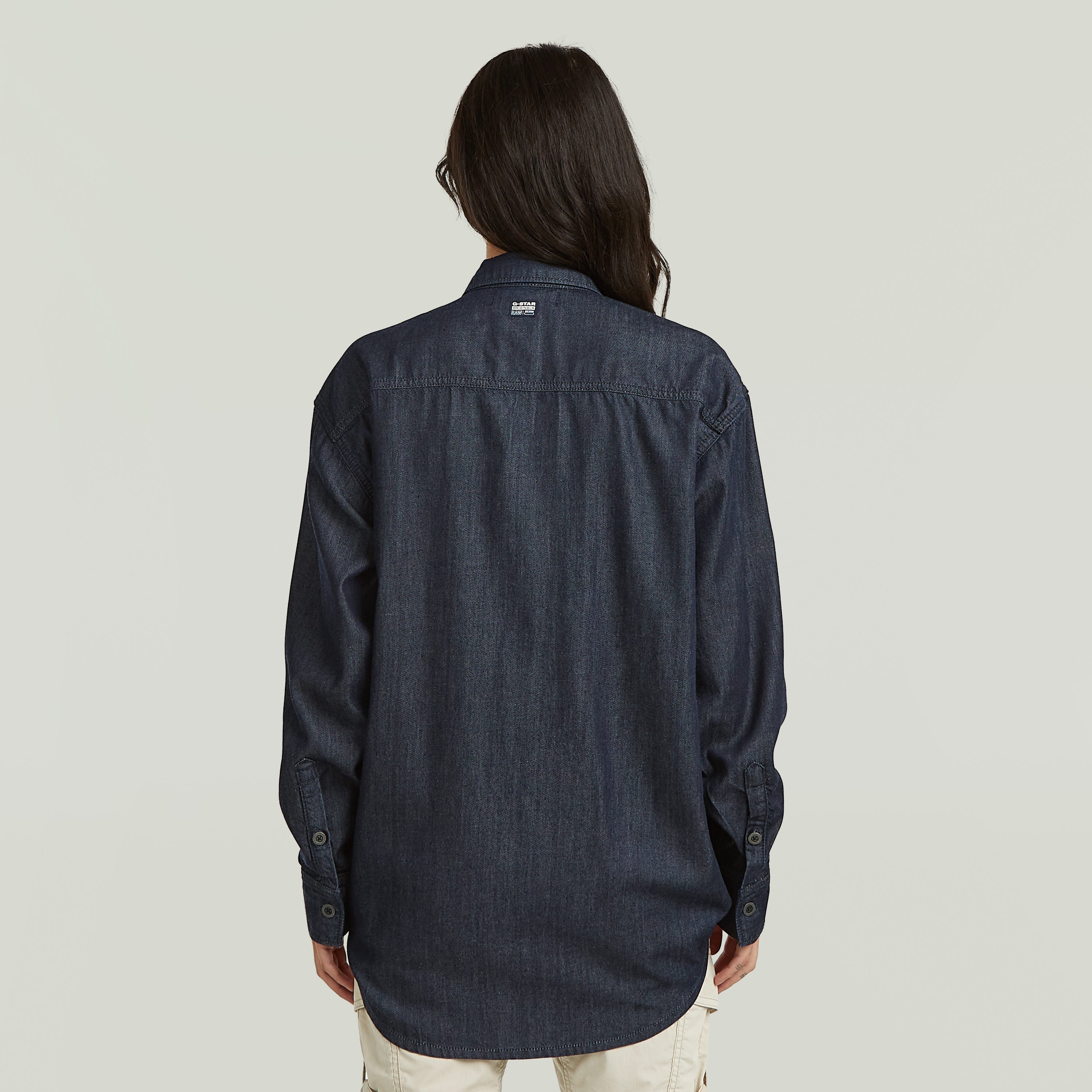 Mujer usando una camisa ligera de estilo relajado, vista desde atrás, en denim oscuro.