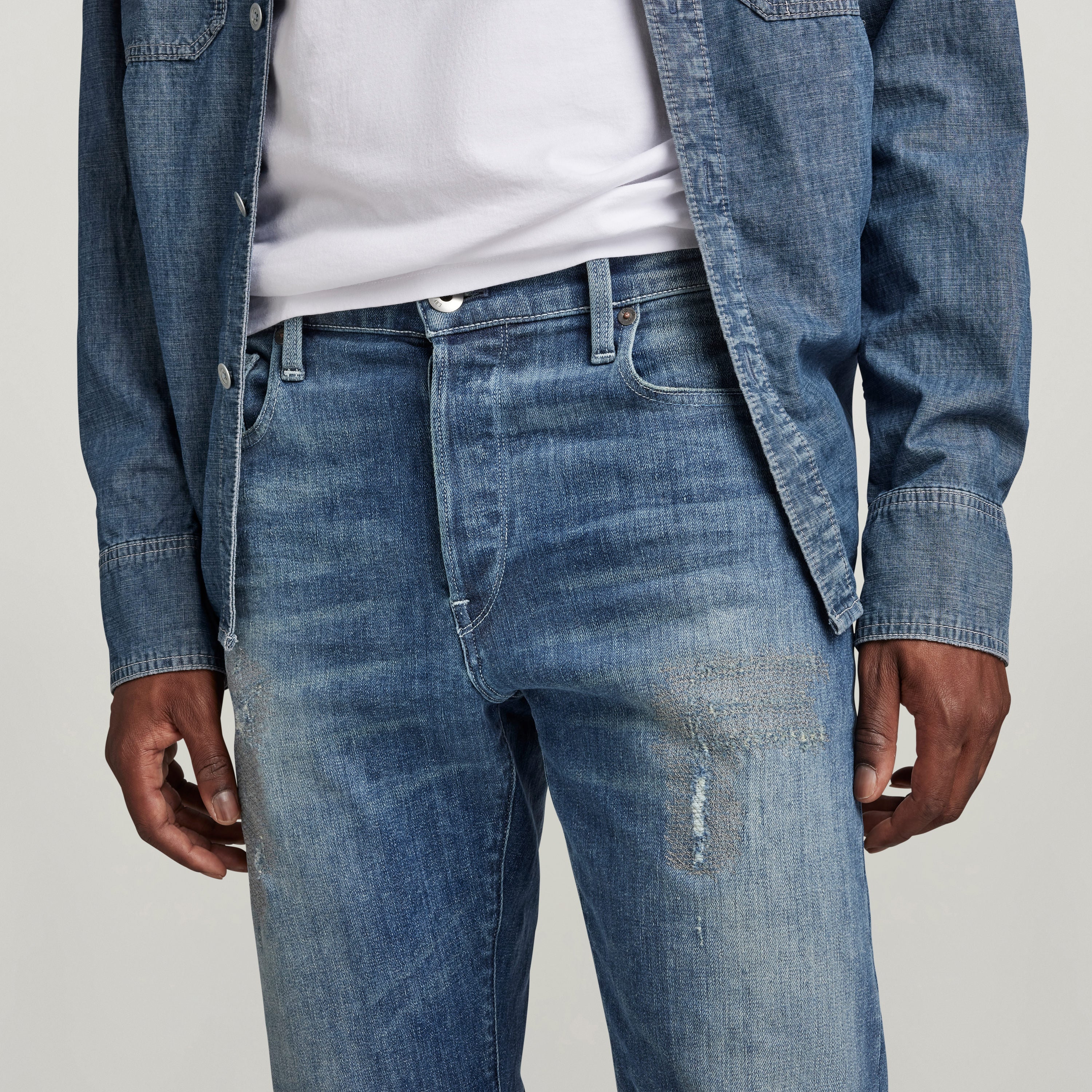 G-Star 3301 Slim jeans in blue denim with distressed detail and button fly, styled with a casual shirt.