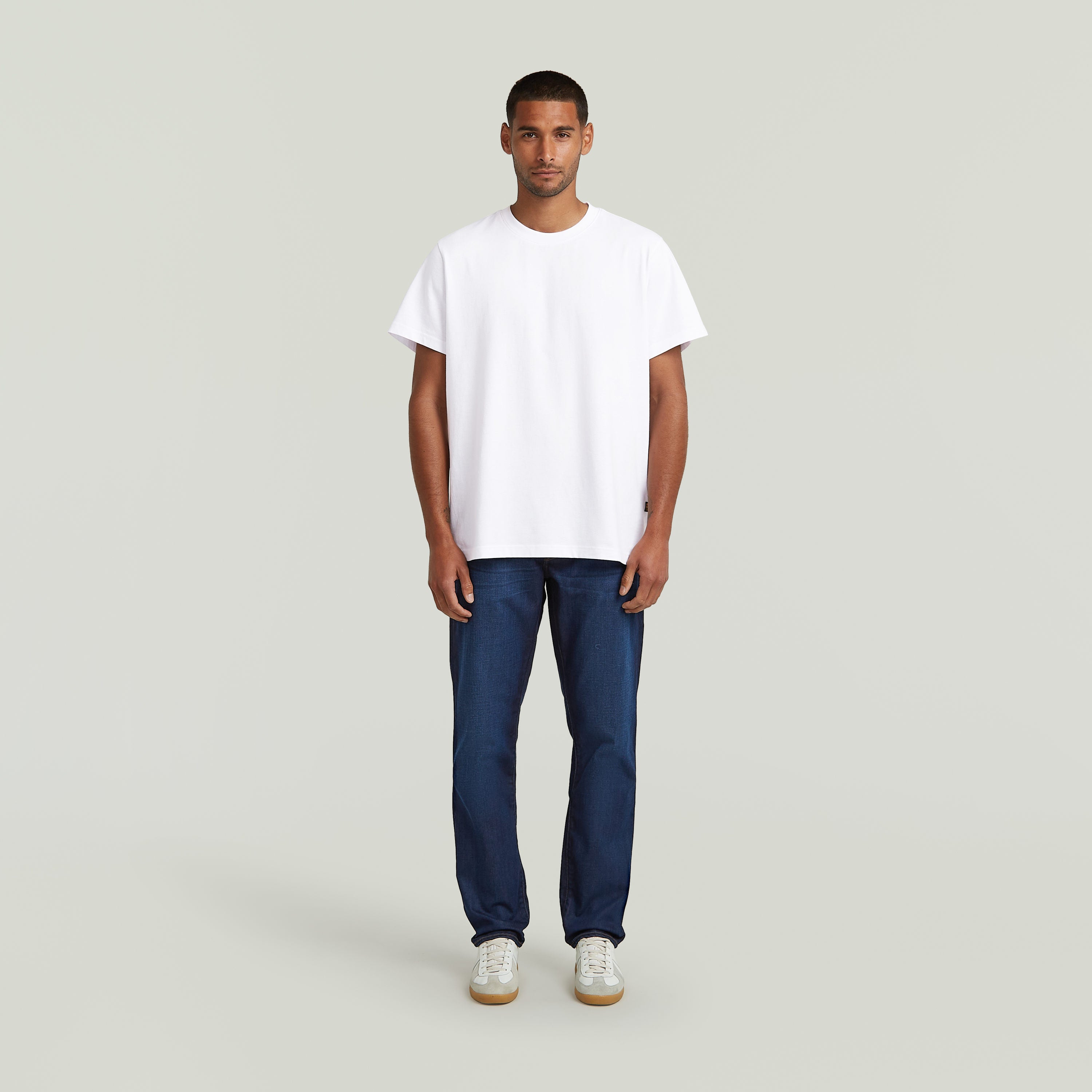 Hombre usando jeans G-Star 3301 Straight y camiseta blanca, con zapatos deportivos en fondo neutro.