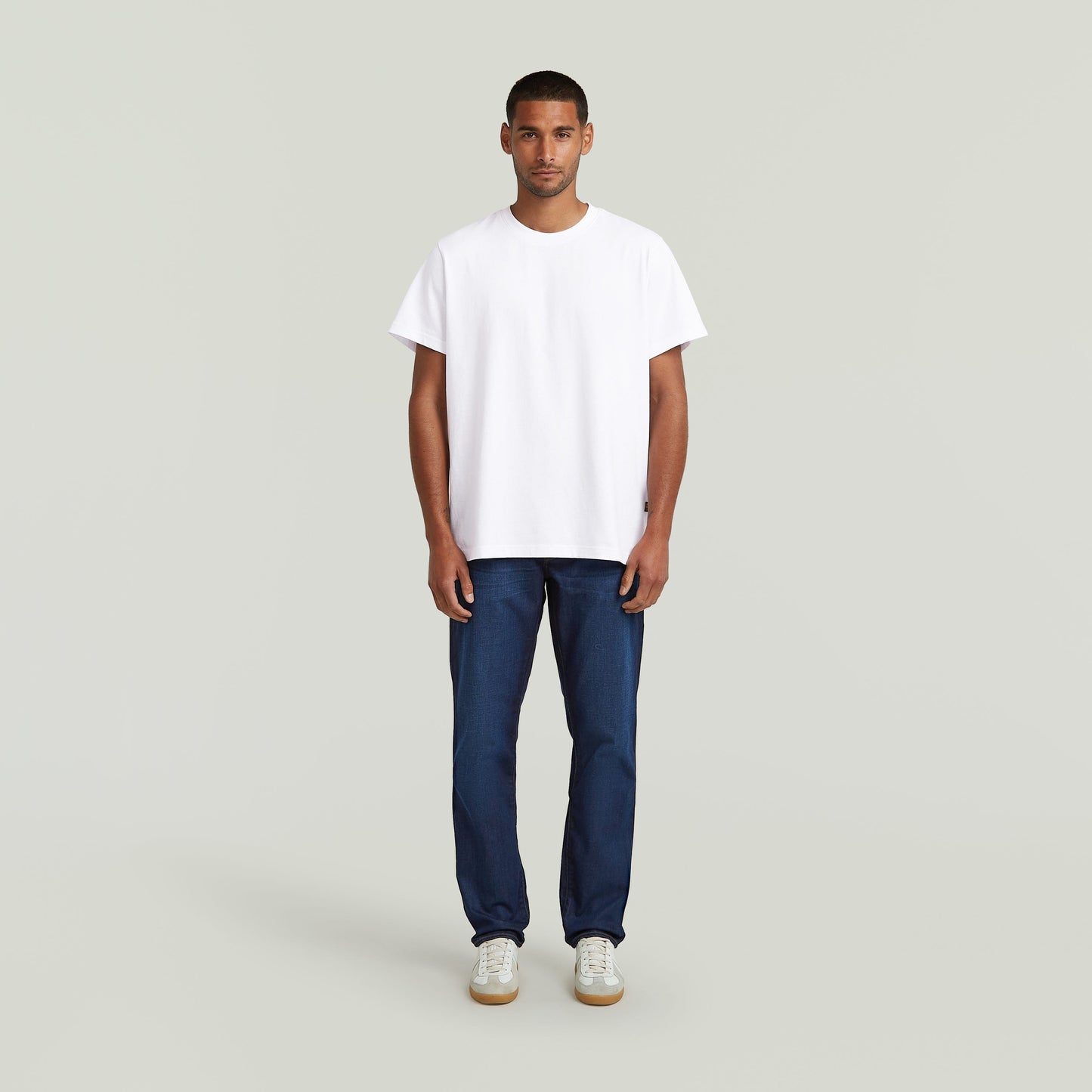 Hombre usando jeans G-Star 3301 Straight y camiseta blanca, con zapatos deportivos en fondo neutro.