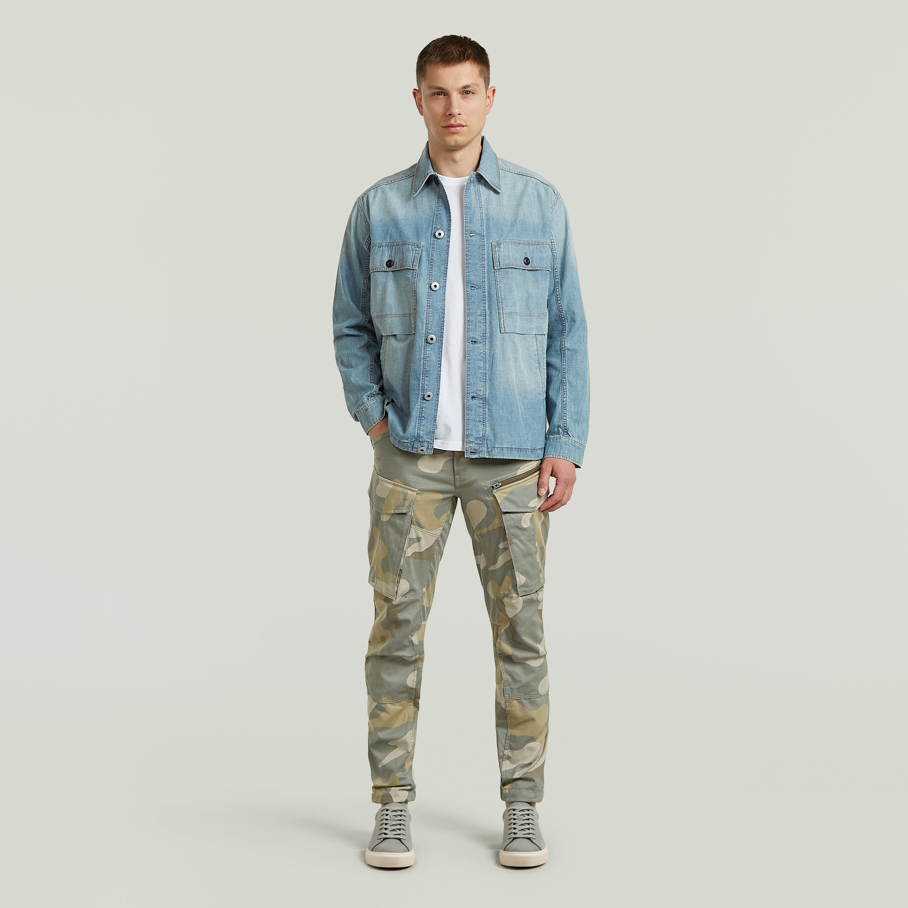 Modelo masculino vistiendo pantalones Rovic Zip 3D tapered pants y chaqueta de mezclilla en fondo neutro.