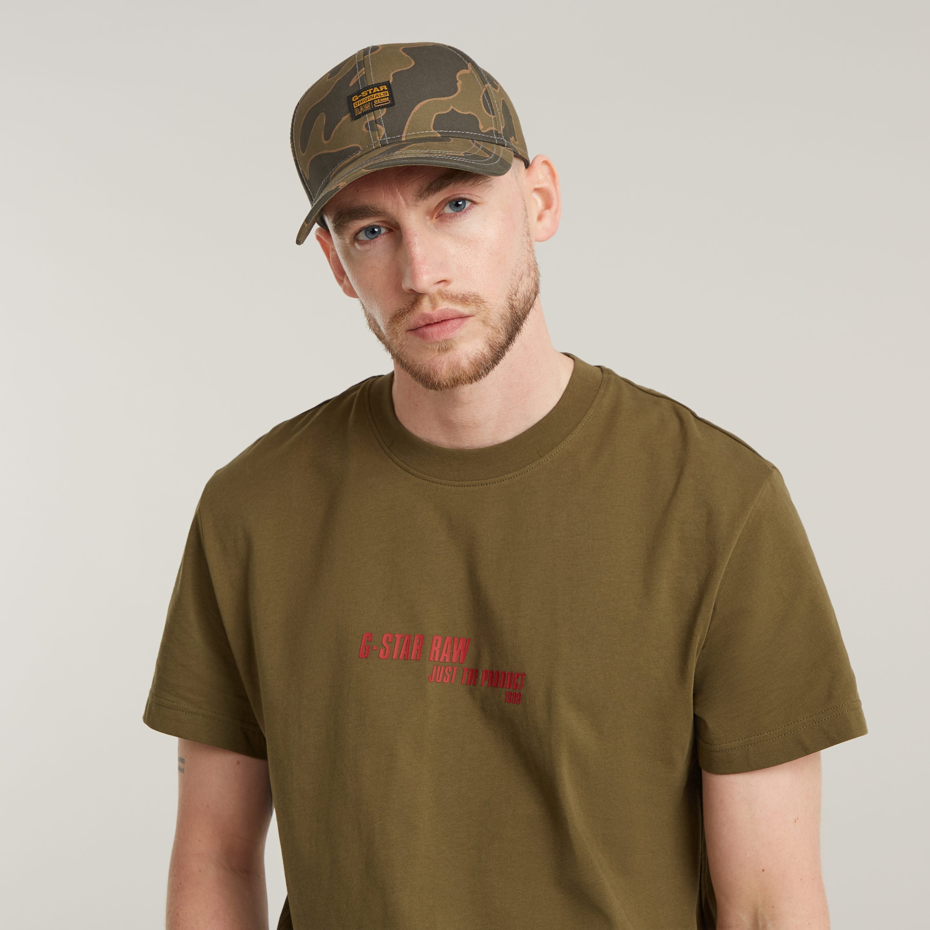 Hombre usando la gorra Originals Baseball con parche tejido y camiseta G-Star en fondo neutro.