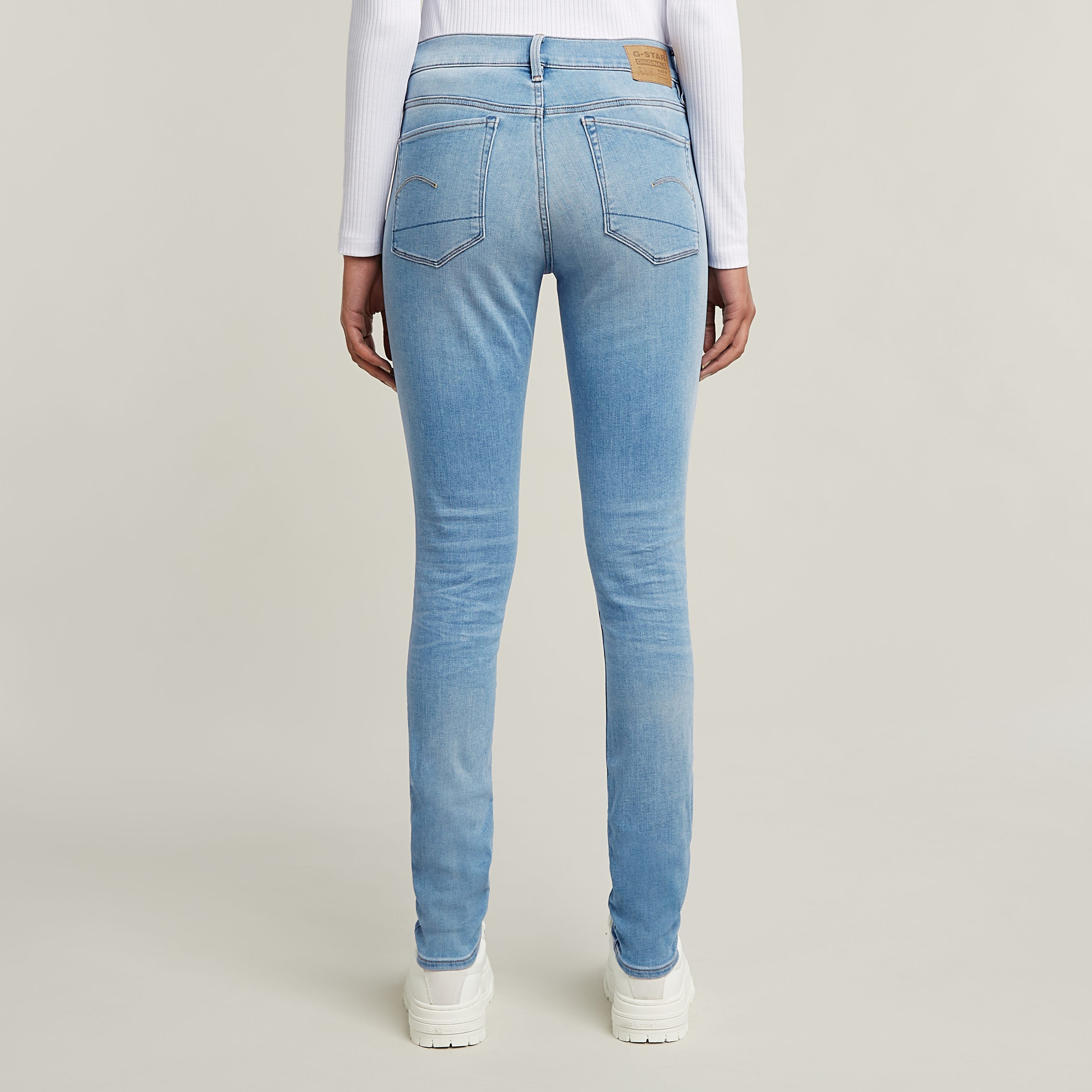 Mujer usando jeans 3301 skinny de corte pitillo en azul claro desde atrás, con detalles clásicos y etiqueta en la parte trasera.