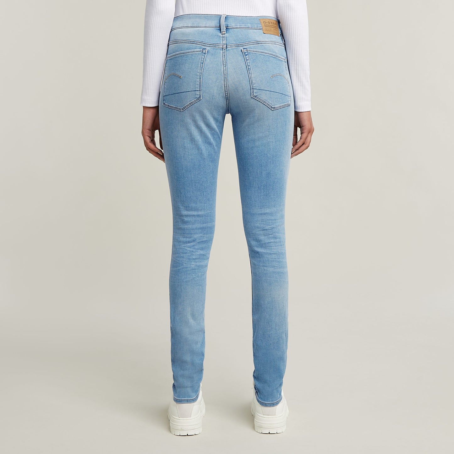 Mujer usando jeans 3301 skinny de corte pitillo en azul claro desde atrás, con detalles clásicos y etiqueta en la parte trasera.