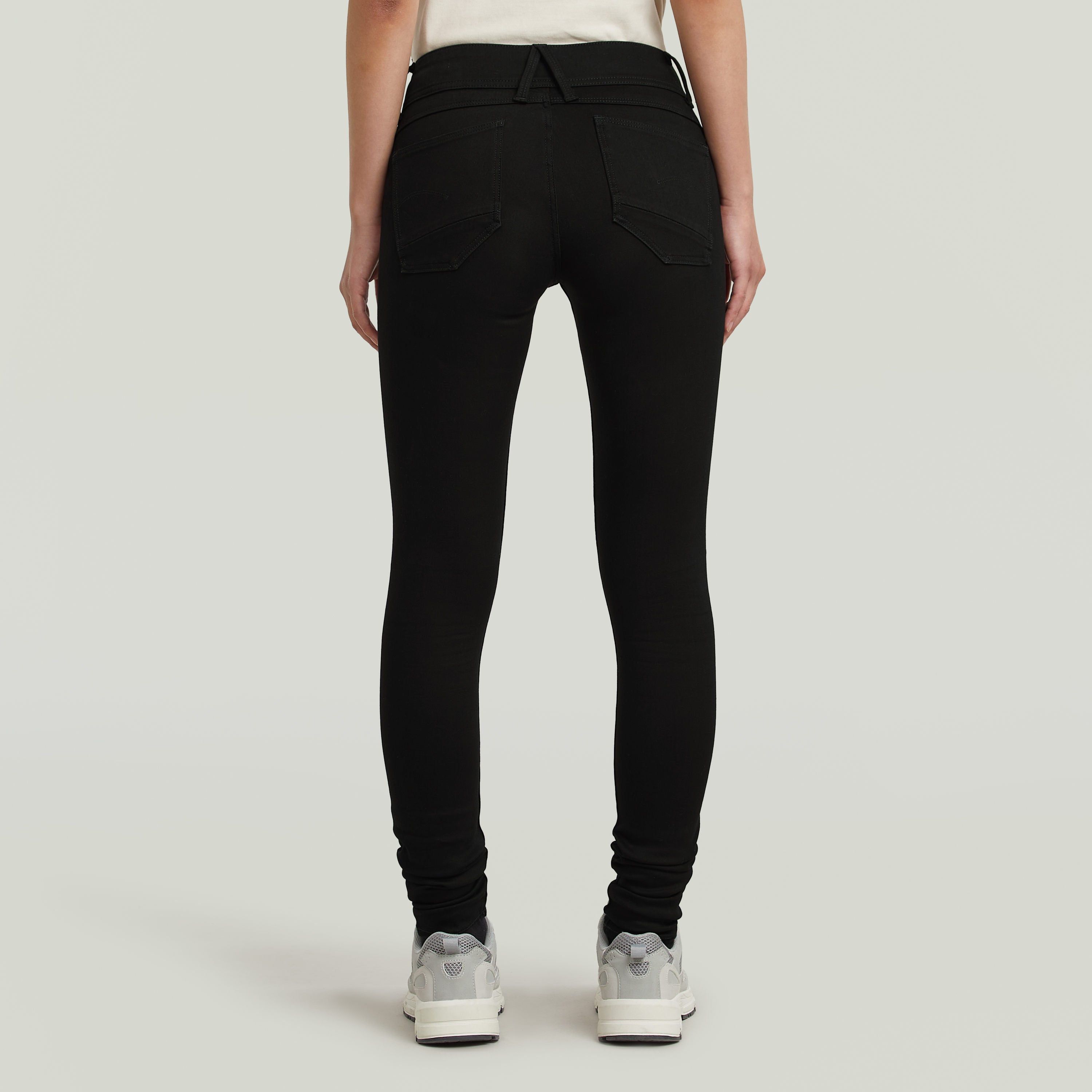 Mujer usando los jeans Lynn super skinny, mostrando la parte trasera del modelo en denim negro ajustado.