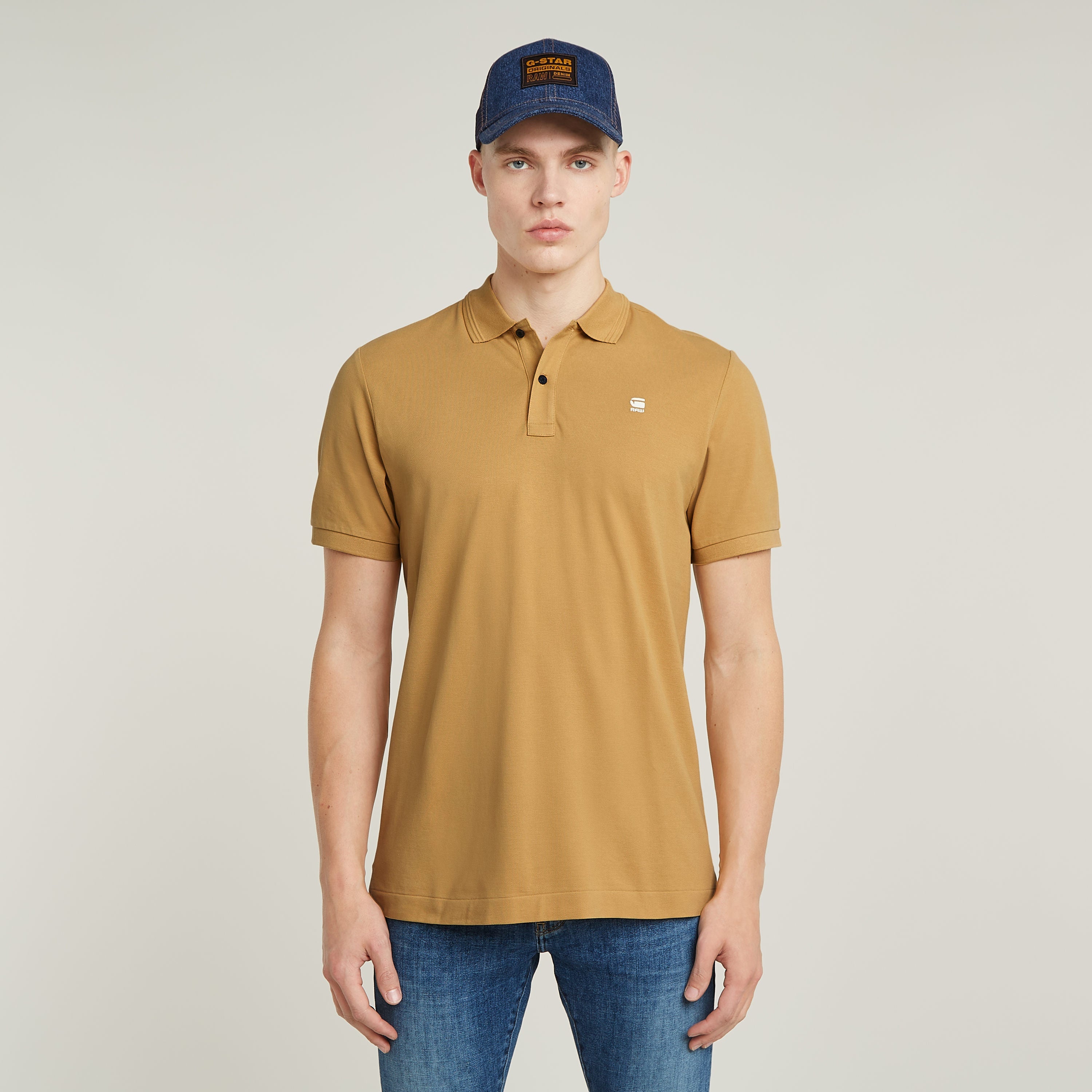 Modelo luciendo el Dunda Slim polo en color marrón con gorra azul, destacando su diseño moderno y cómodo.