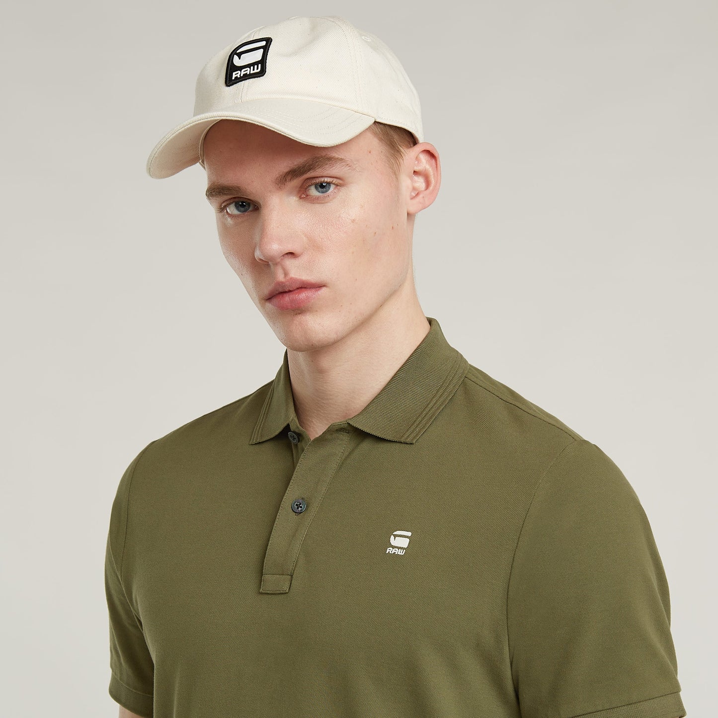 Modelo usando la Dunda Slim Polo Shirt en color oliva, con sombrero blanco y logotipo en la parte frontal.