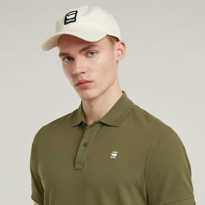 Modelo usando la Dunda Slim Polo Shirt en color oliva, con sombrero blanco y logotipo en la parte frontal.