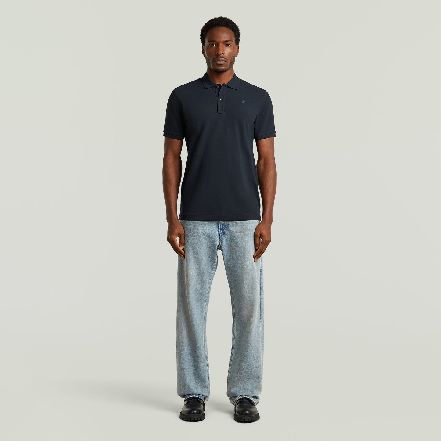 Modelo usando Polo Dunda Slim fit polo shirt color azul oscuro, combinado con jeans y calzado negro.
