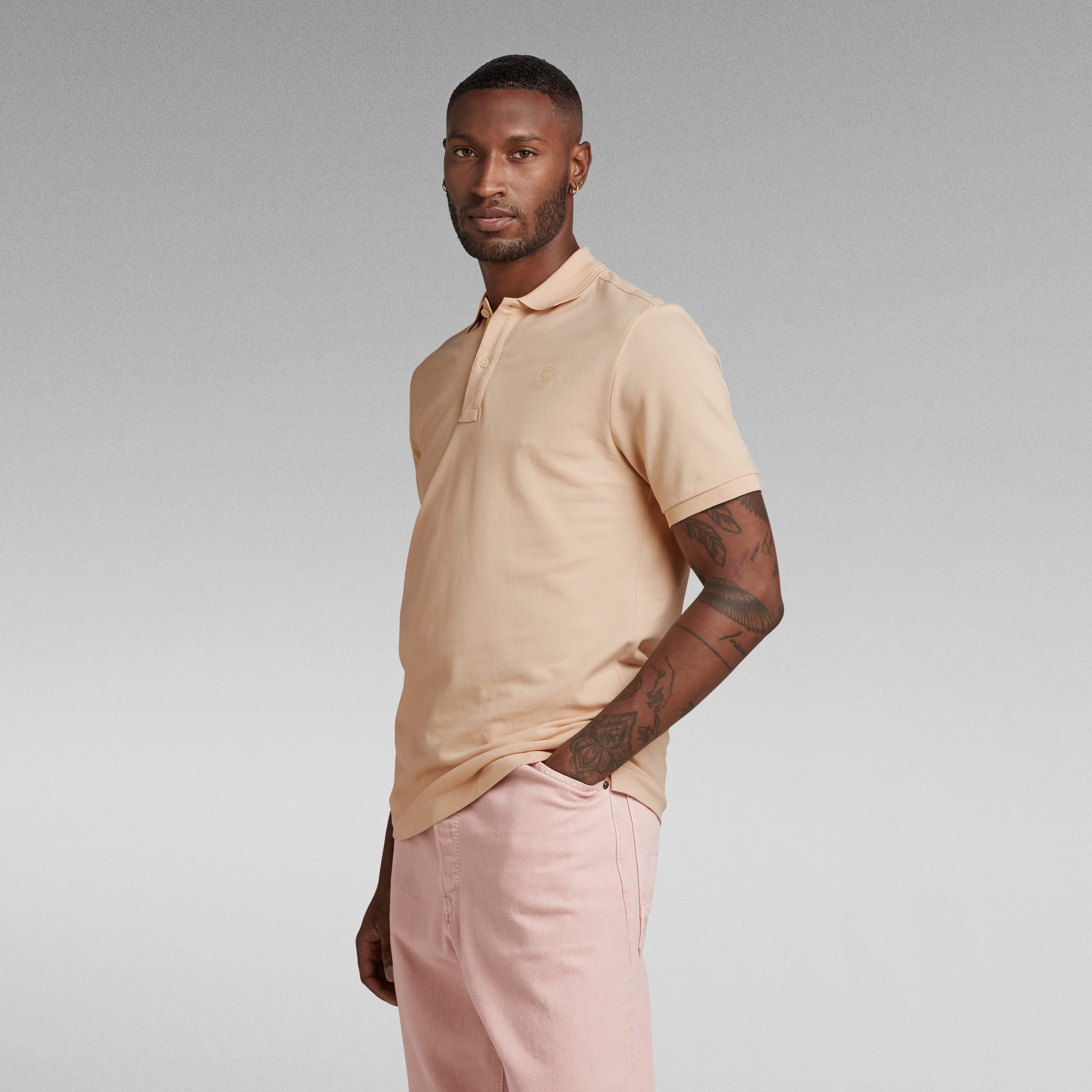 Hombre vistiendo un polo Dunda Slim con cuello acanalado en color beige y pantalones rosa.