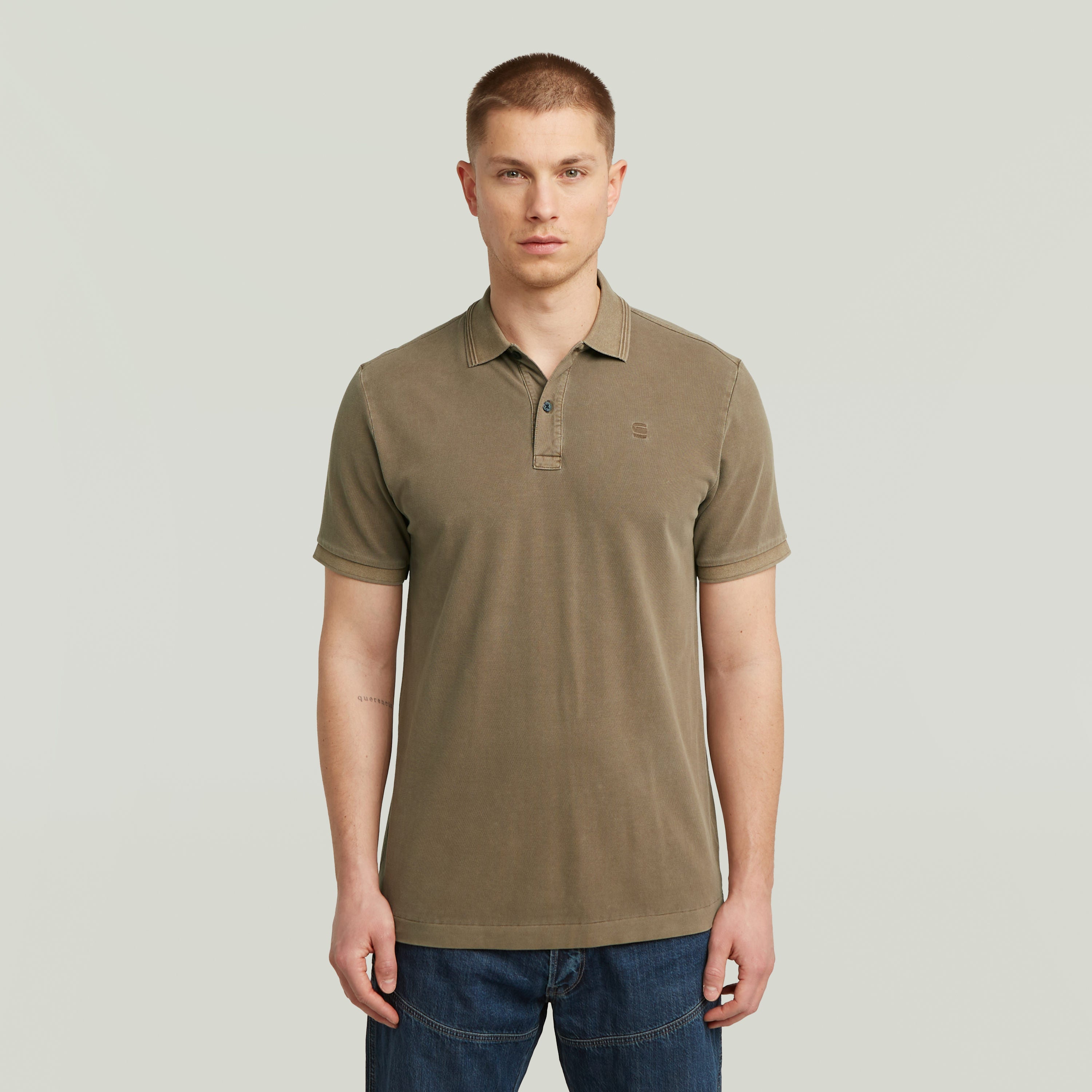 Modelo con el Polo Dunda Overdyed Slim fit polo shirt en color marrón claro, con cuello tradicional y botón.
