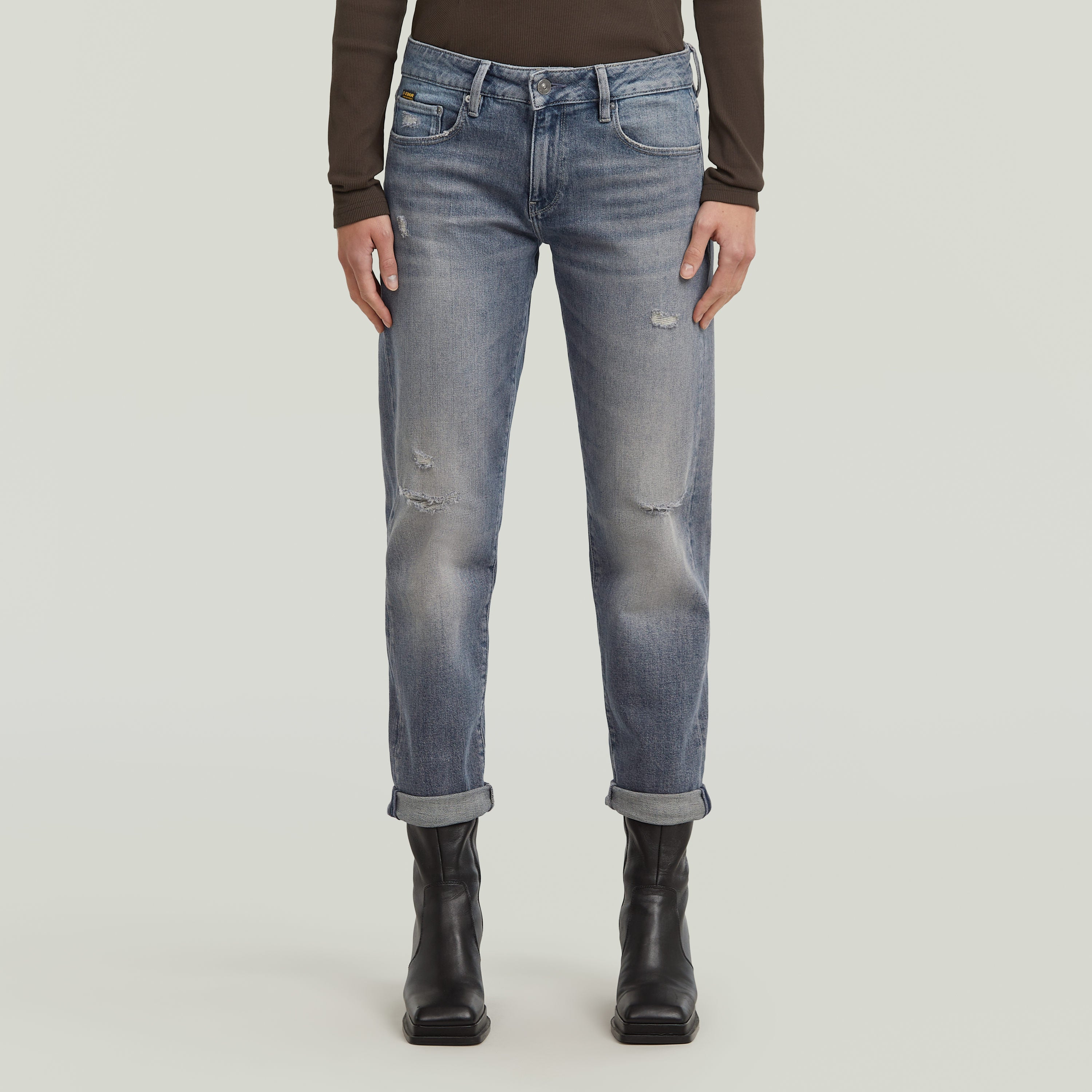 Mujer usando low rise boyfriend jeans de color azul claro, con dobladillo plegado y botines negros.