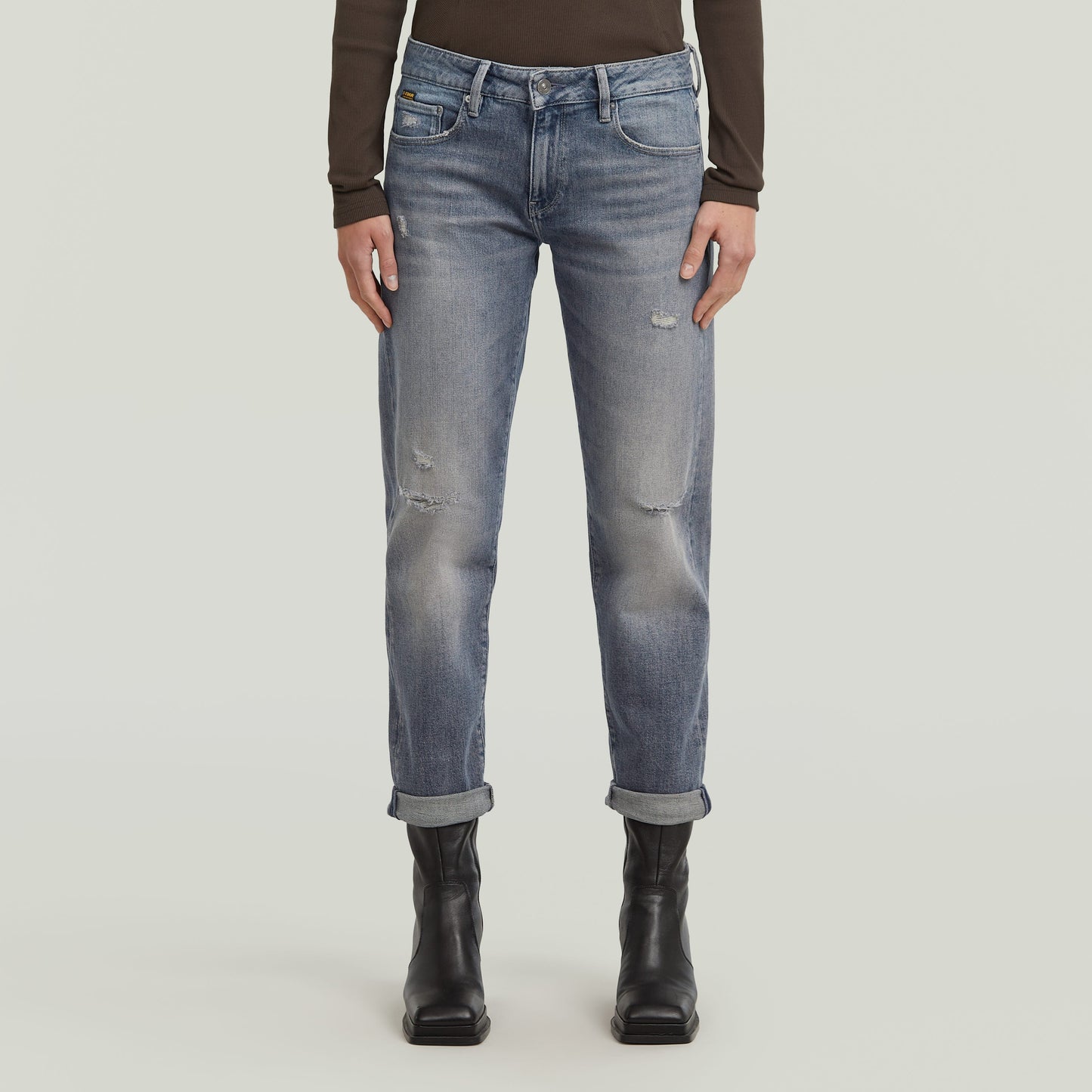 Mujer usando low rise boyfriend jeans de color azul claro, con dobladillo plegado y botines negros.
