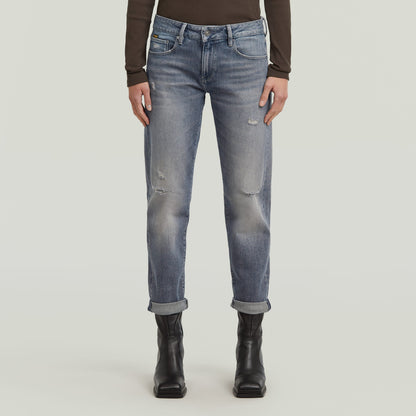 Mujer usando low rise boyfriend jeans de color azul claro, con dobladillo plegado y botines negros.