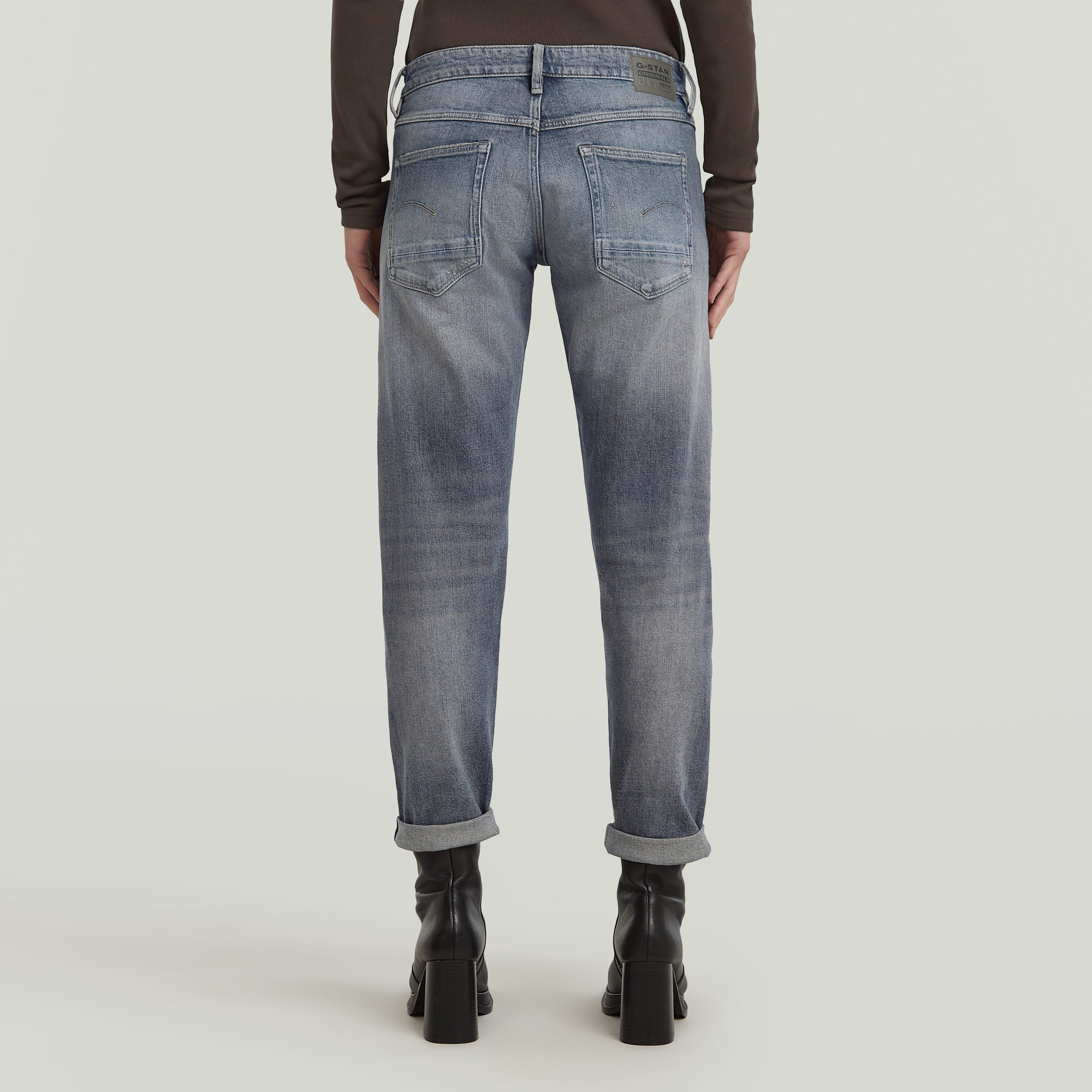 Back view of low rise boyfriend jeans with relaxed fit and rolled hem in light blue.