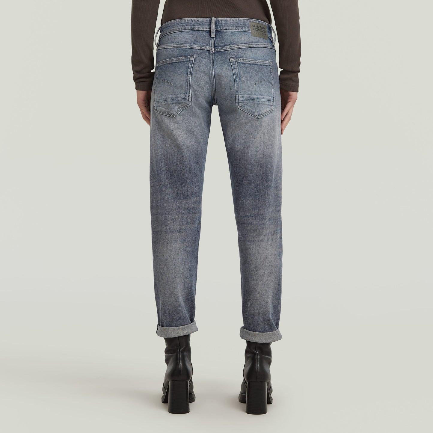 Back view of low rise boyfriend jeans with relaxed fit and rolled hem in light blue.